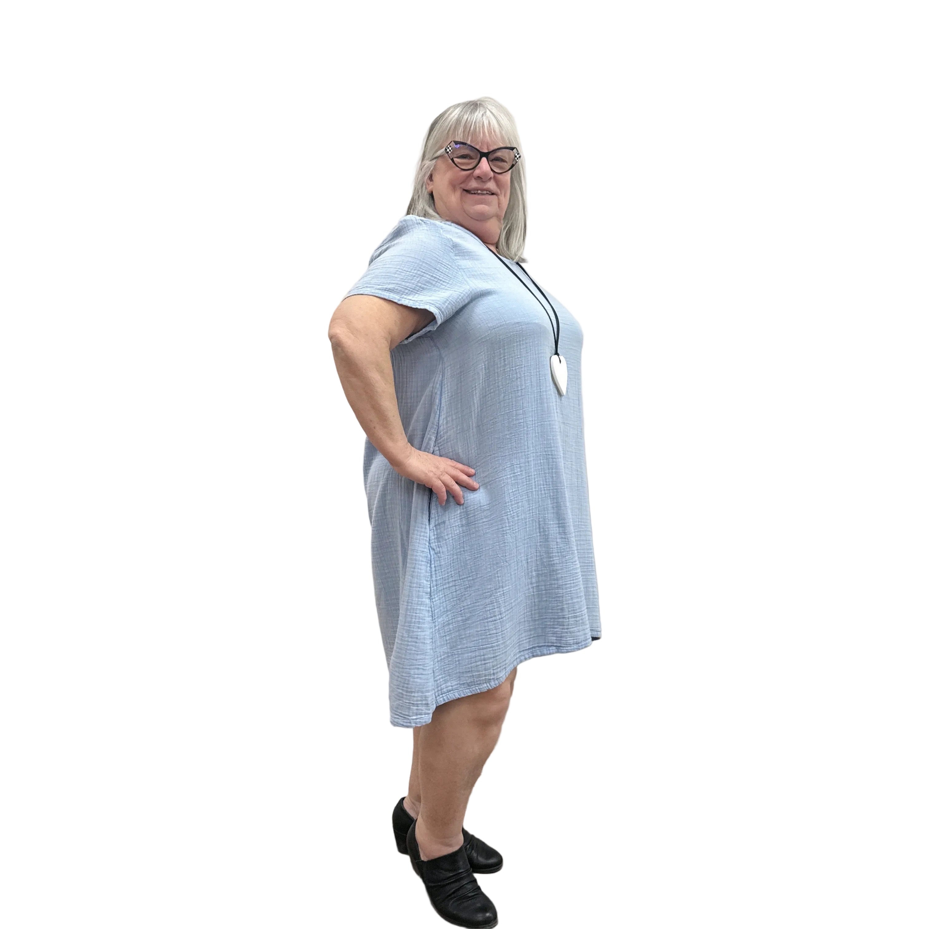 Woman wearing a light blue Papa Passport dress against a plain wall.