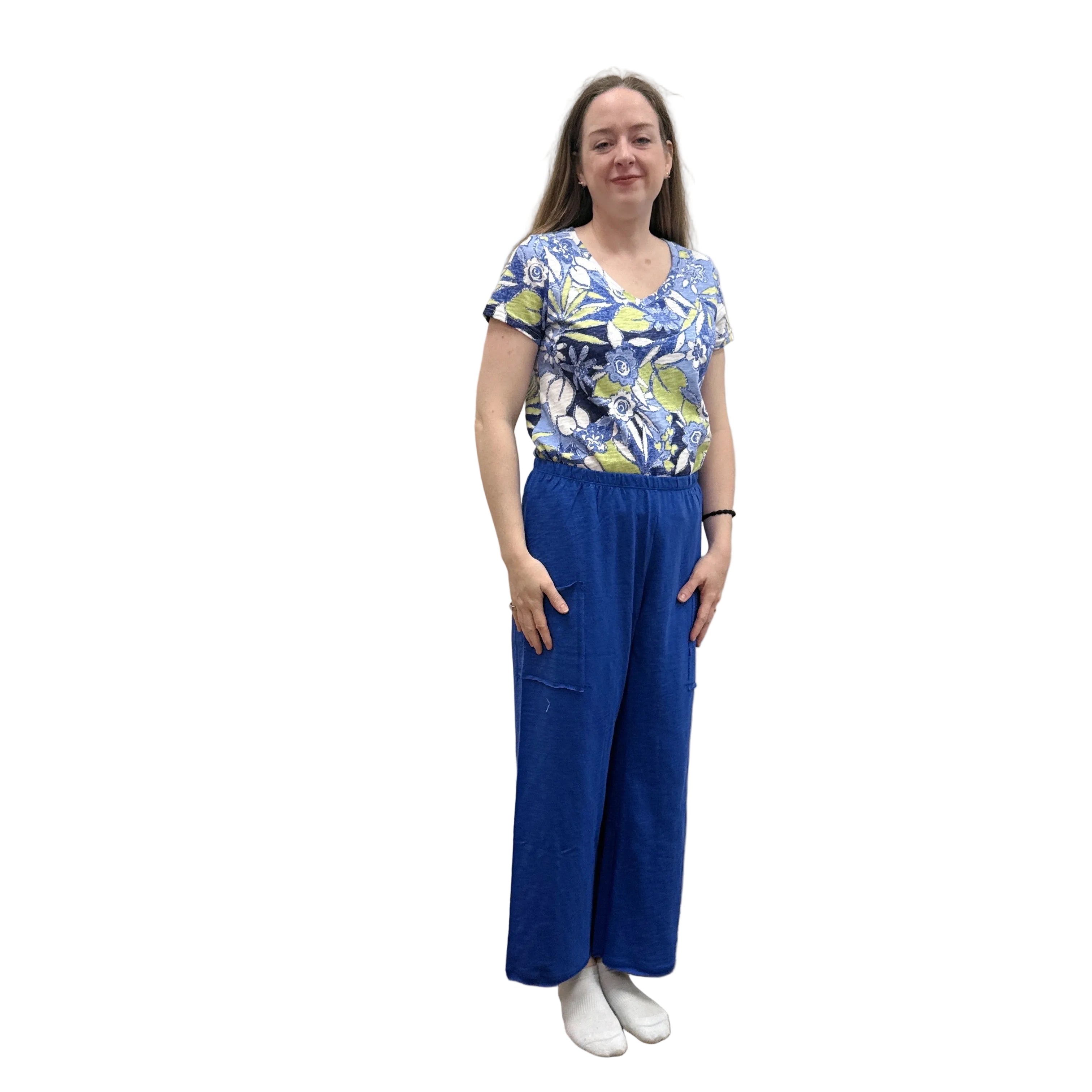 Woman wearing a blue floral top and blue Papa Pocket Flood pants standing against a plain wall.