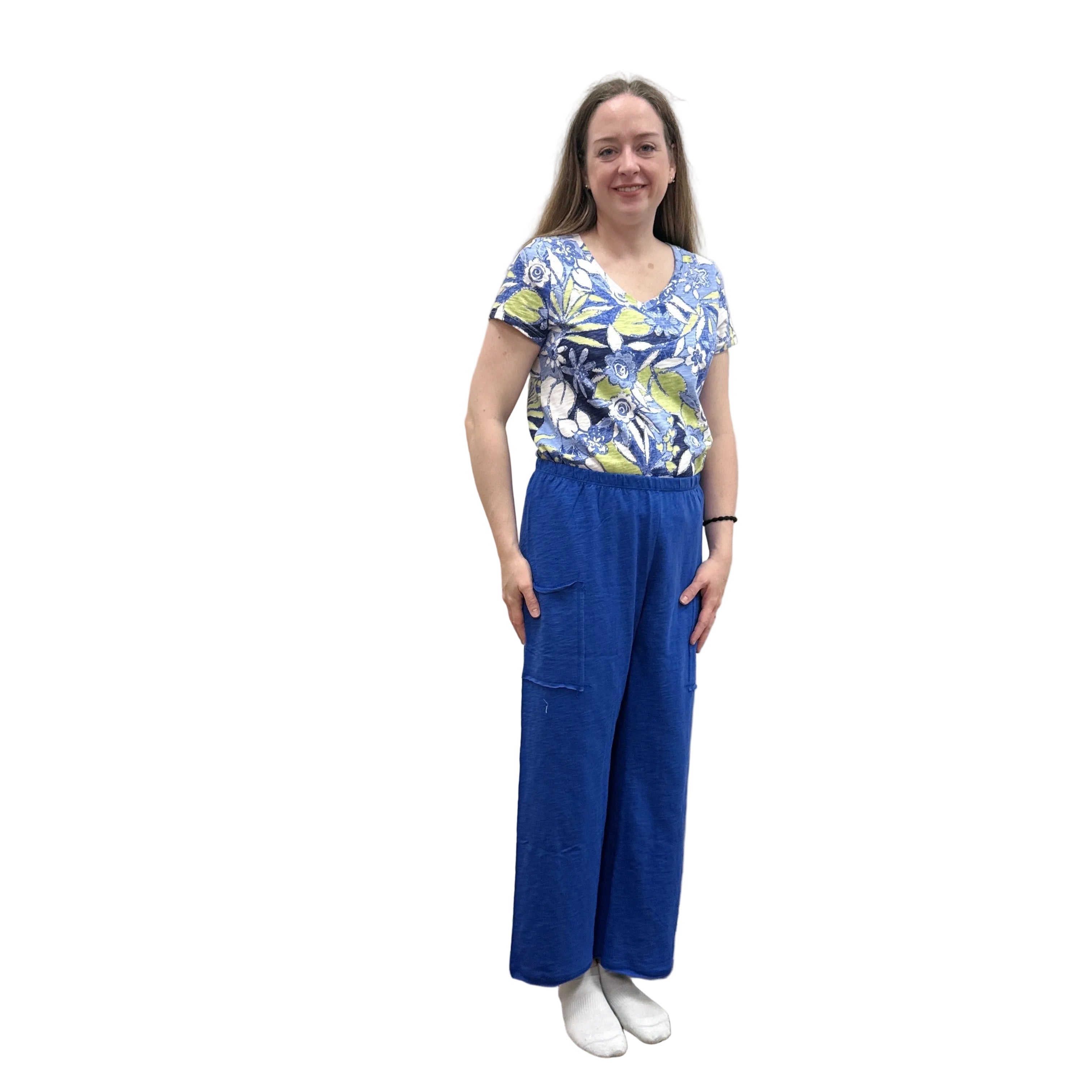 Woman wearing a blue floral top and blue Papa Pocket Flood pants standing against a plain wall.