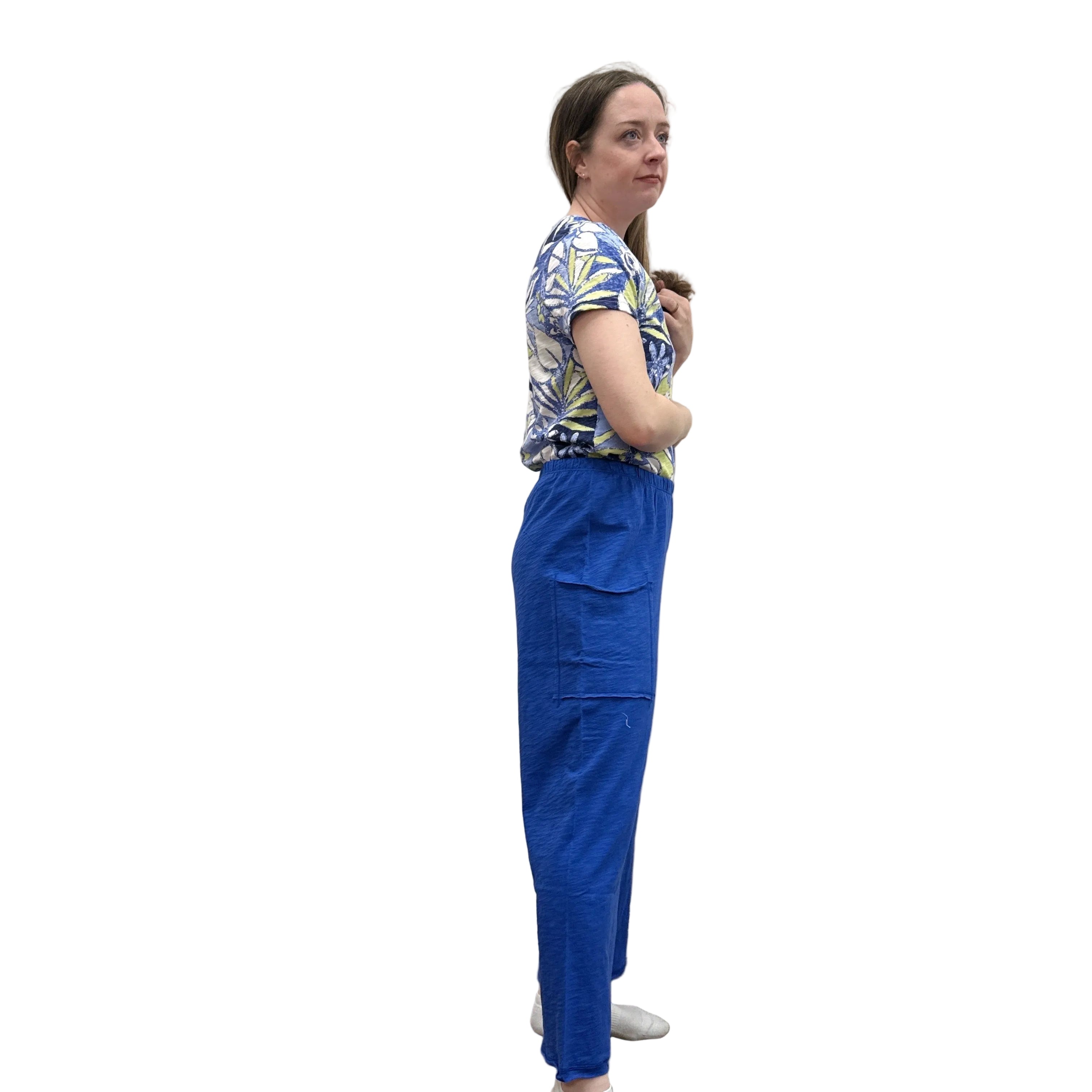 Woman wearing a blue floral top and blue Papa Pocket Flood pants standing against a plain wall.