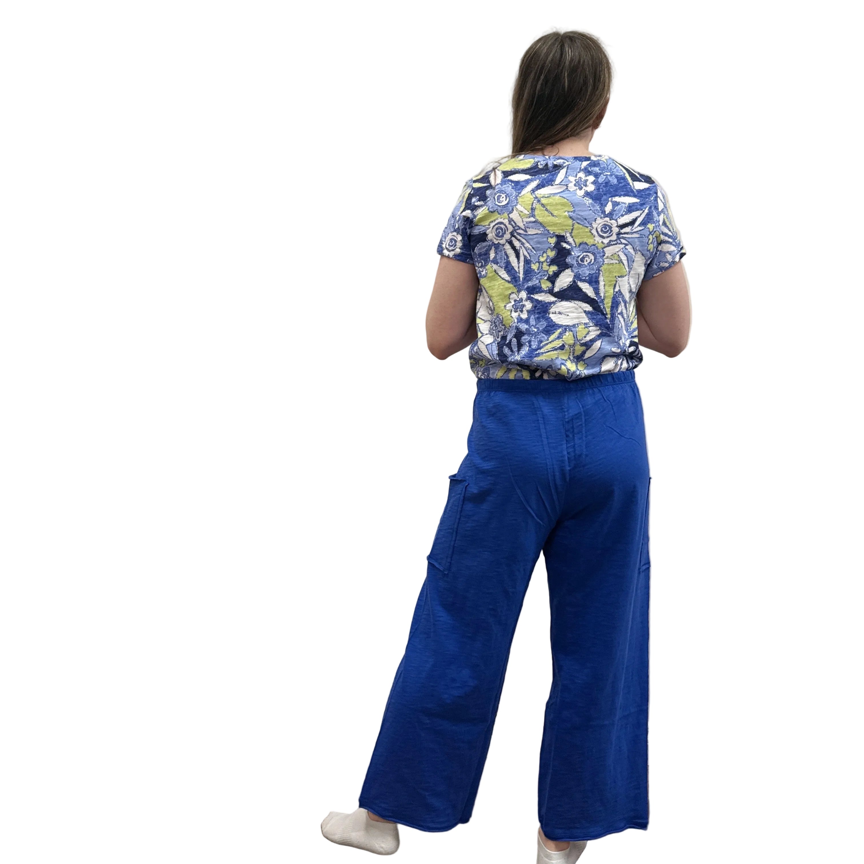 Woman wearing a blue floral top and blue Papa Pocket Flood pants standing against a plain wall.