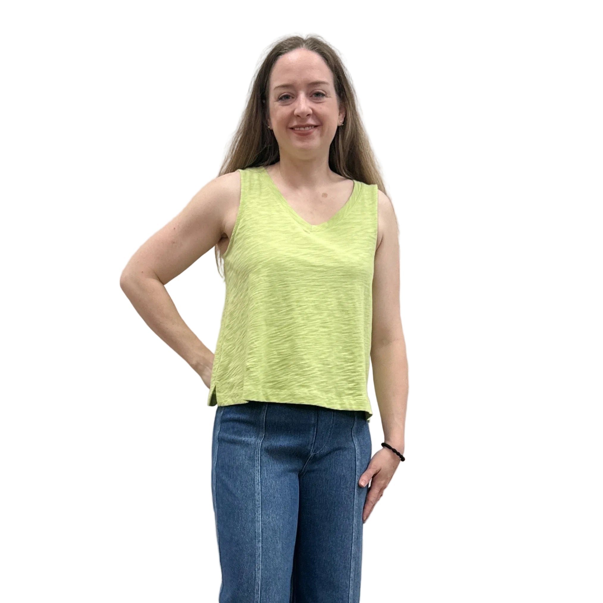 Woman wearing a green sleeveless Papa V-Neck Tank top and blue jeans standing against a plain wall.