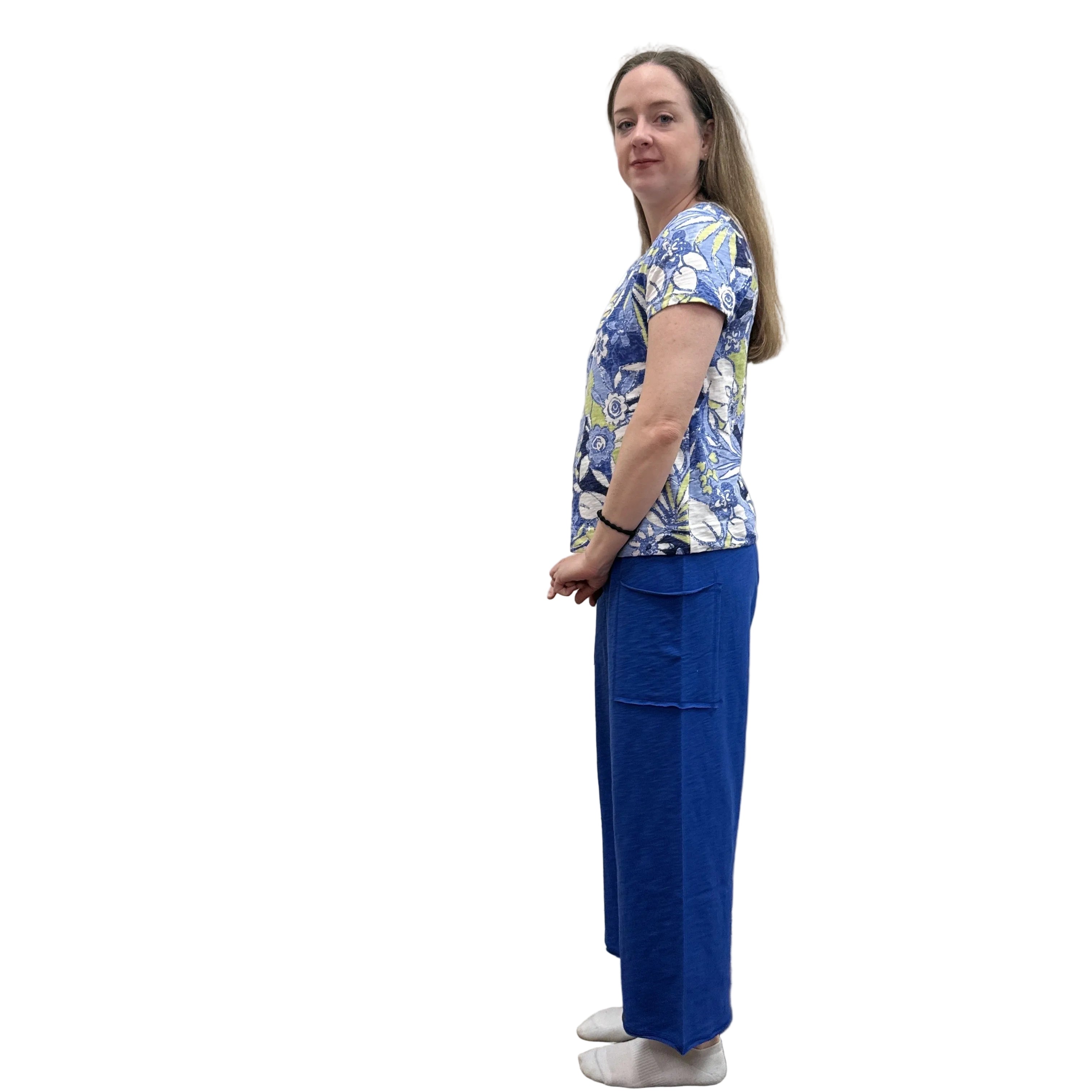 Person wearing a blue floral Papa V Neck top and blue pants standing against a plain wall.