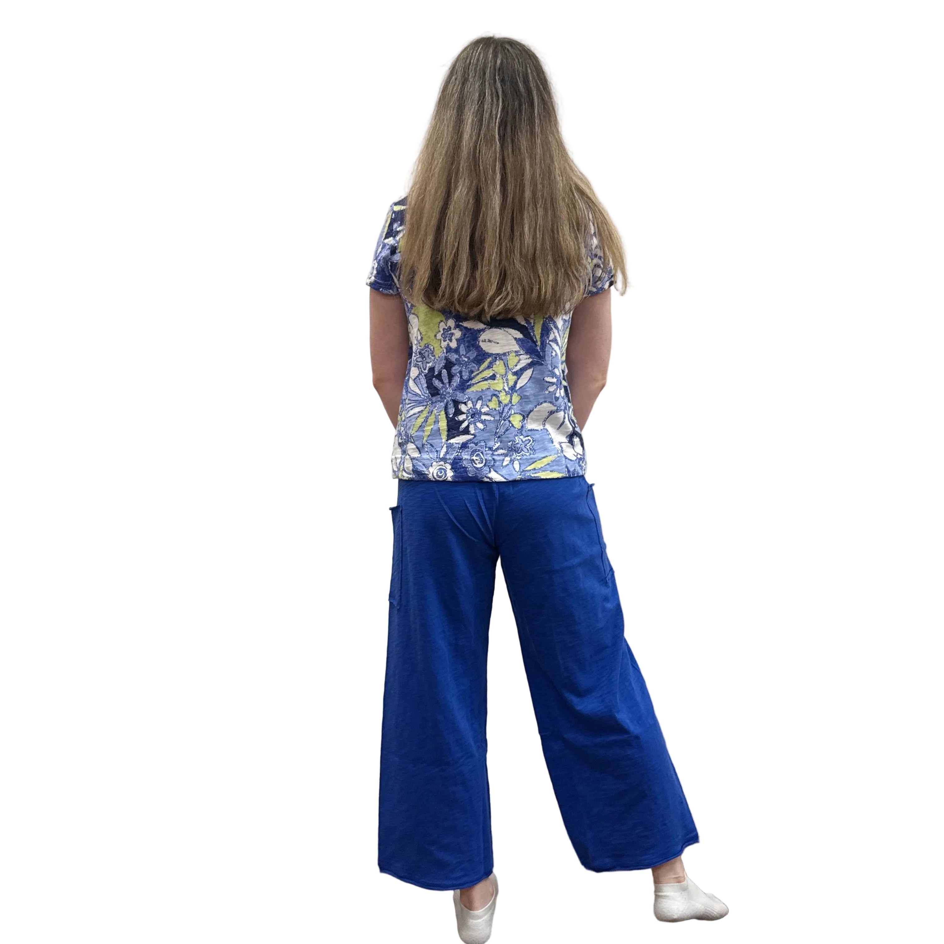 Person wearing a blue floral Papa V Neck top and blue pants standing against a plain wall.