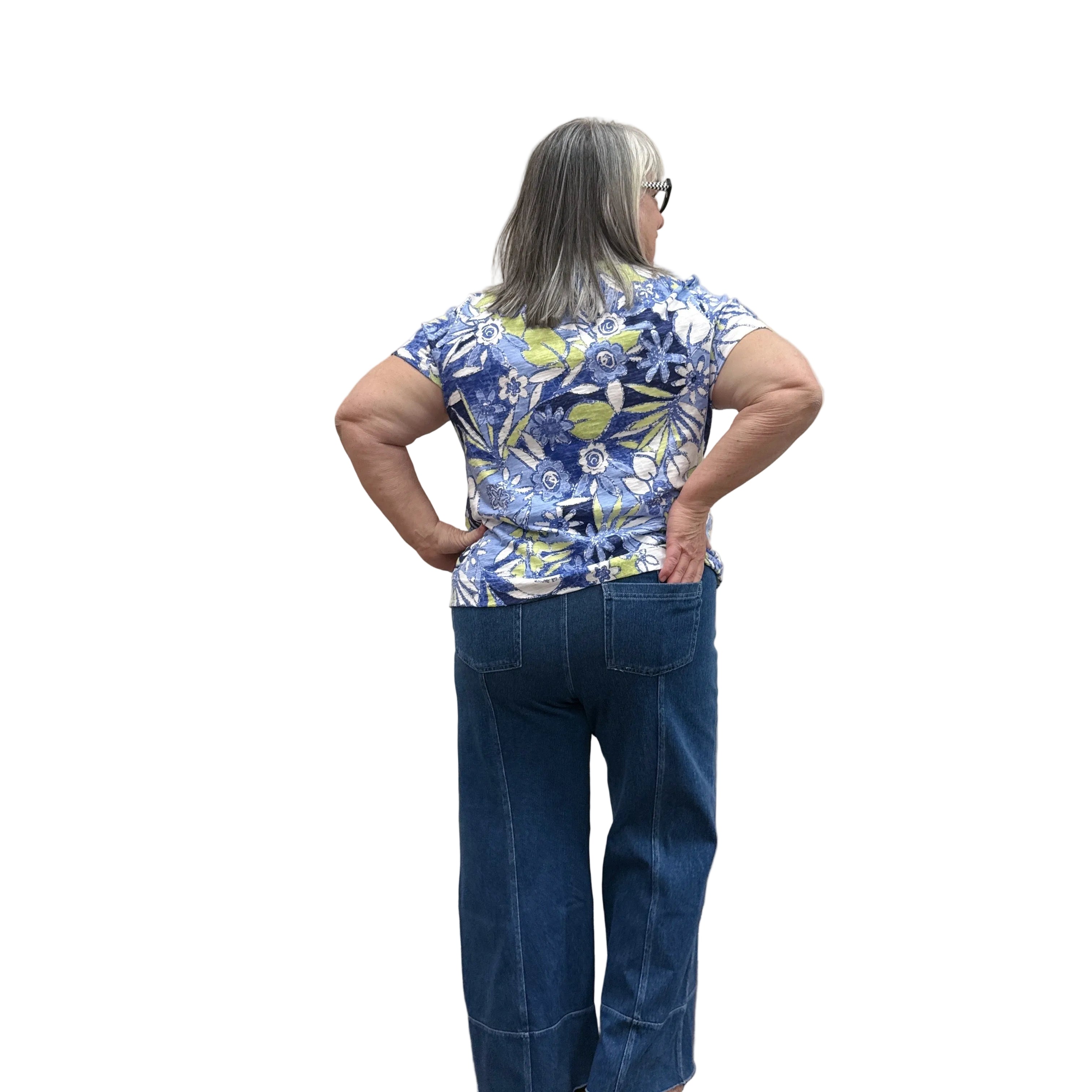 Person wearing a blue floral top and jeans standing against a plain wall.