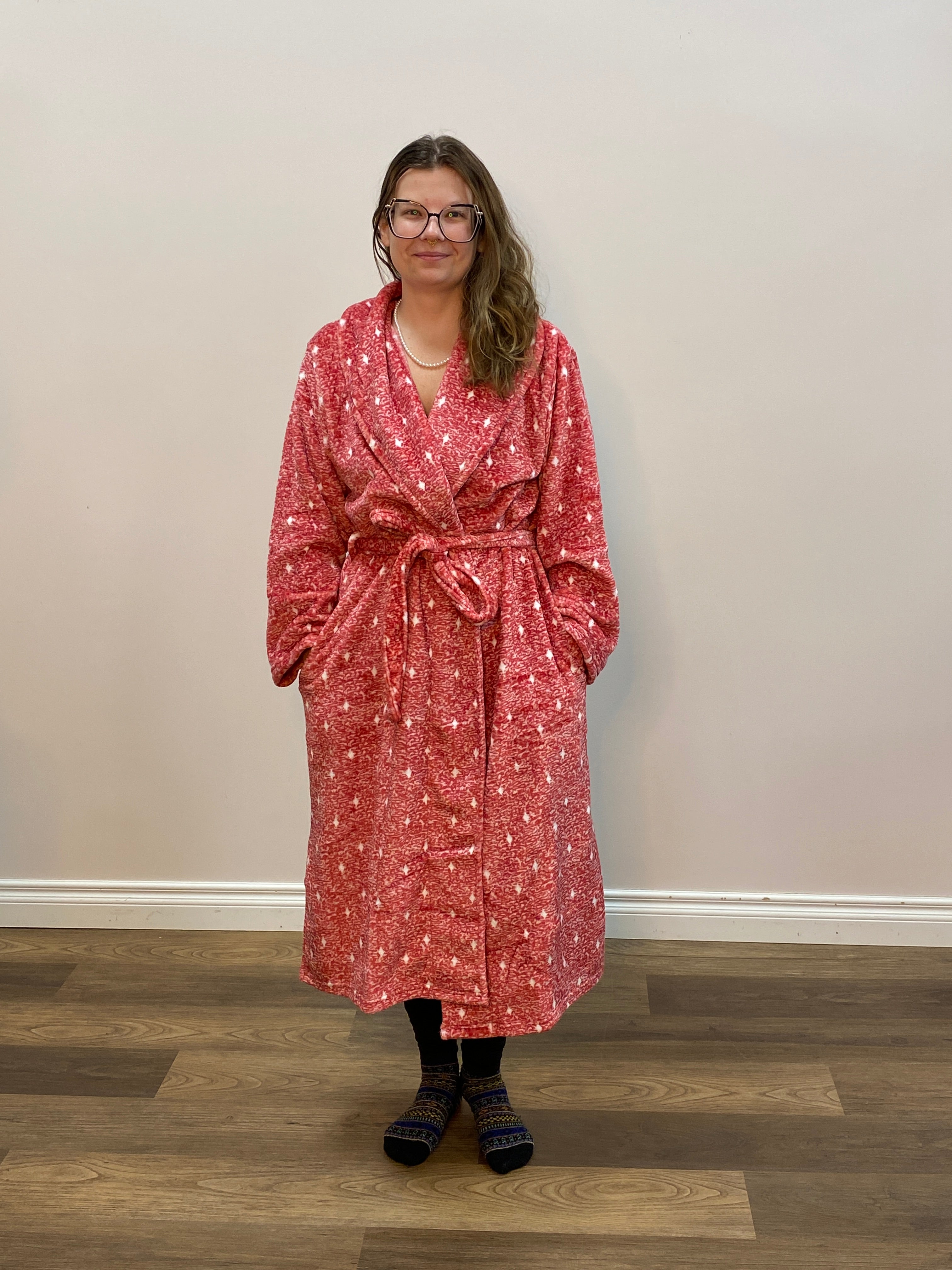 Person wearing a red and white robe standing in a room with wooden flooring.