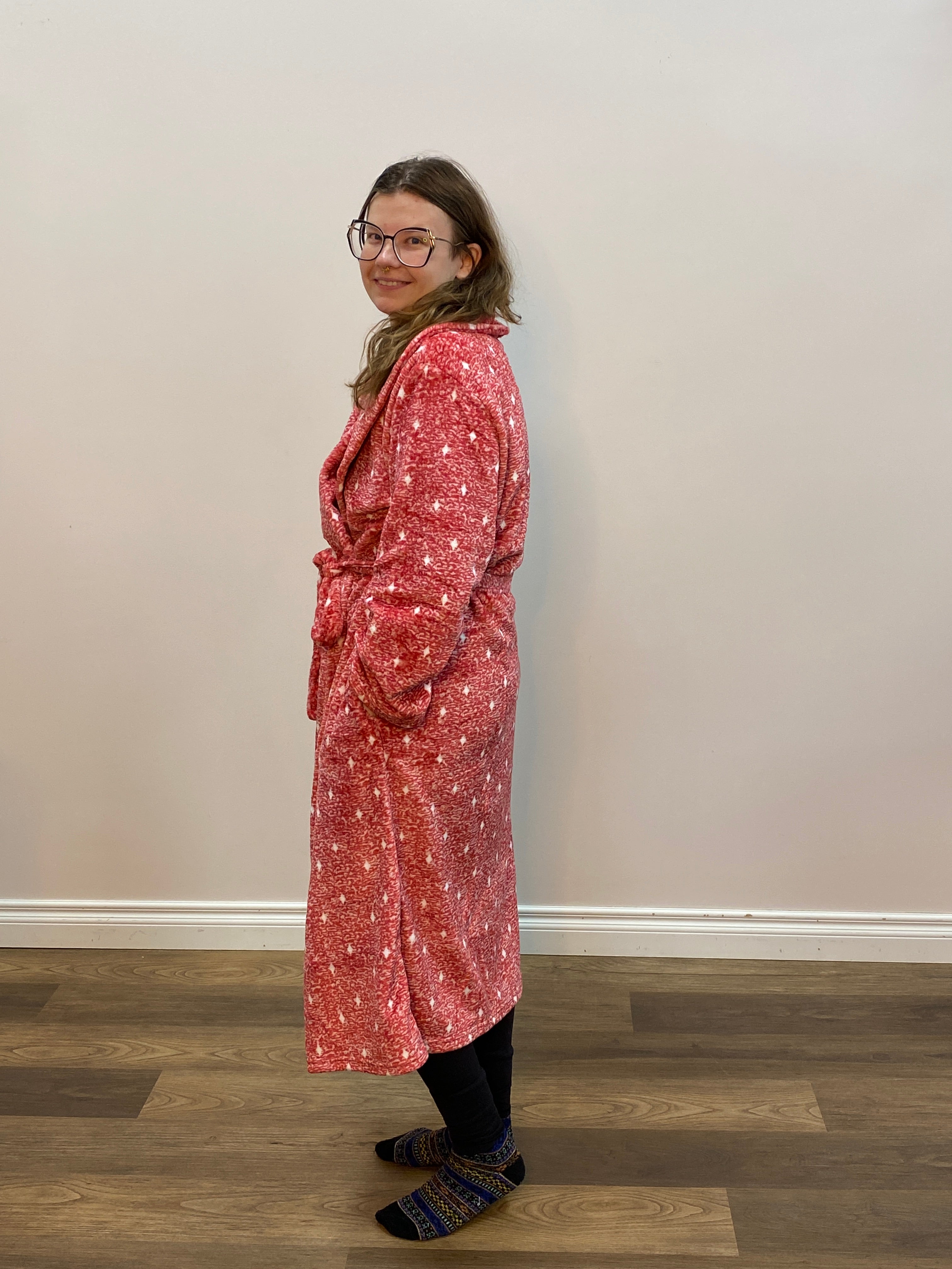 Person wearing a red patterned robe standing in front of a white wall.