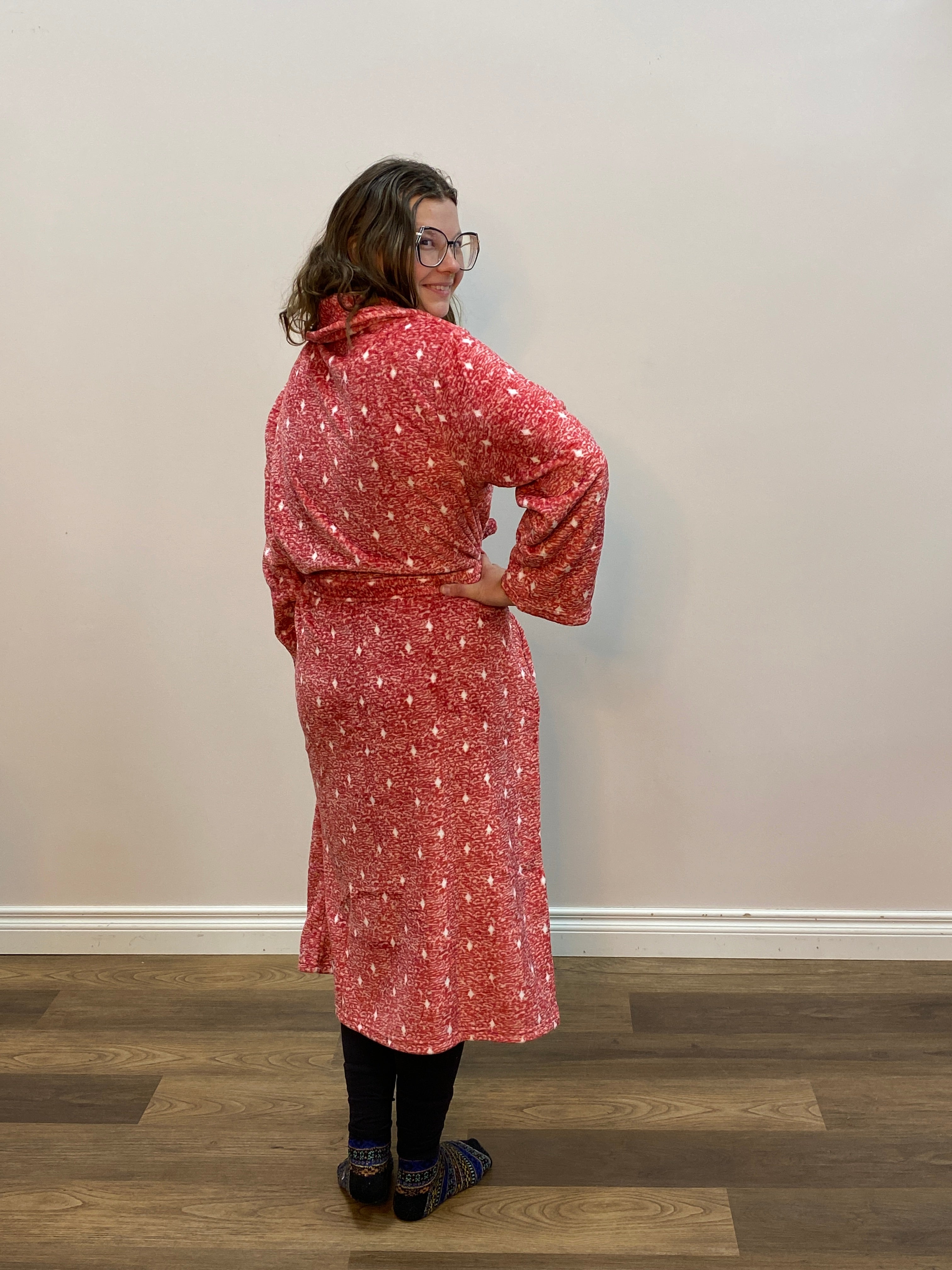Person wearing a red patterned robe standing in front of a white wall.