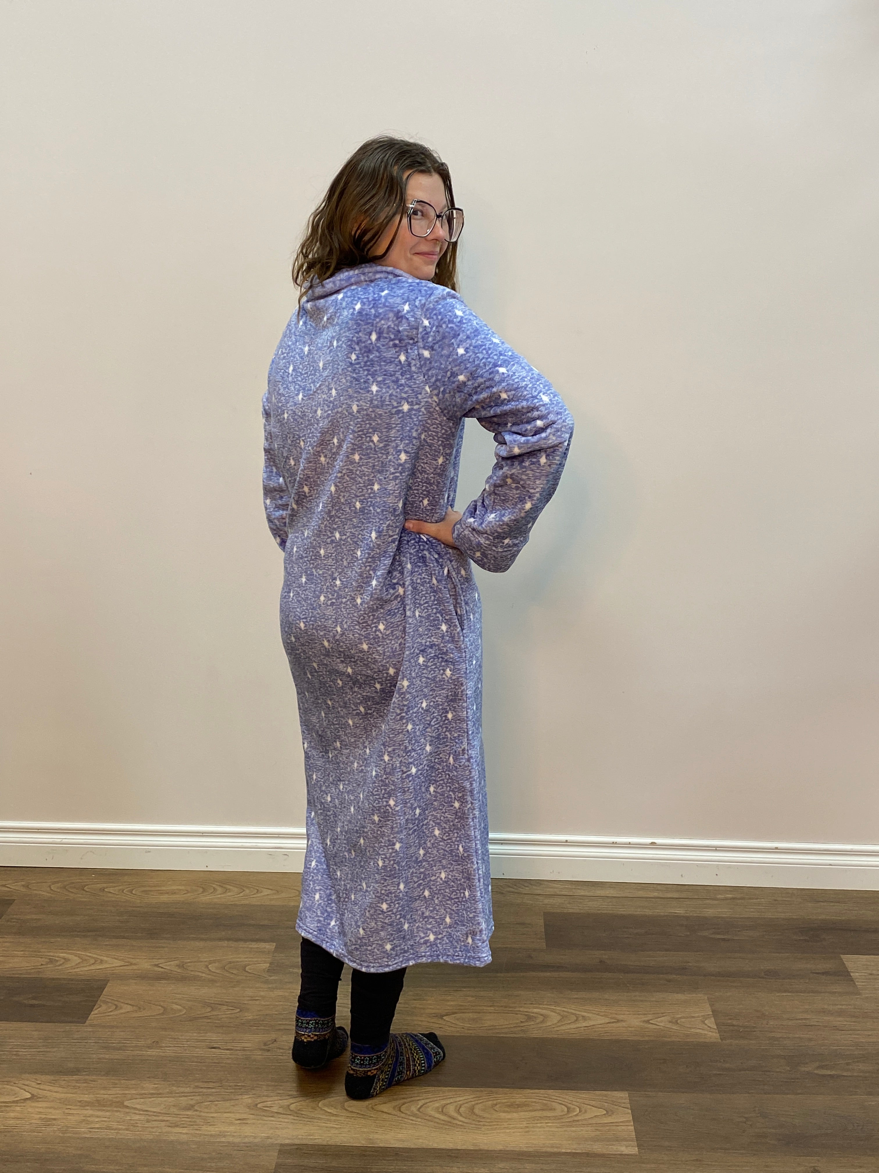 Person wearing a long, light blue robe with a pattern, standing against a plain wall.