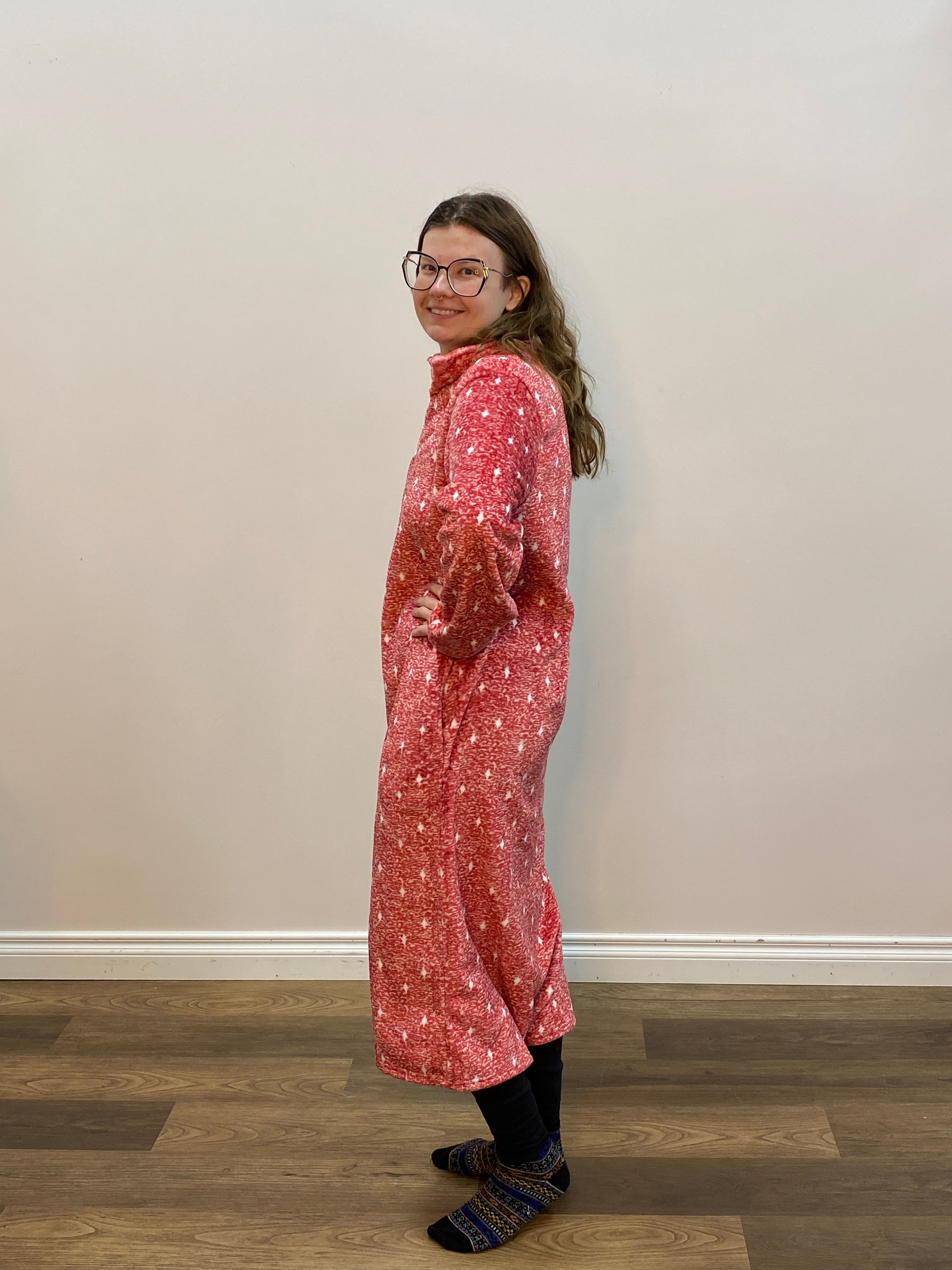 Person wearing a red patterned robe standing against a white wall.