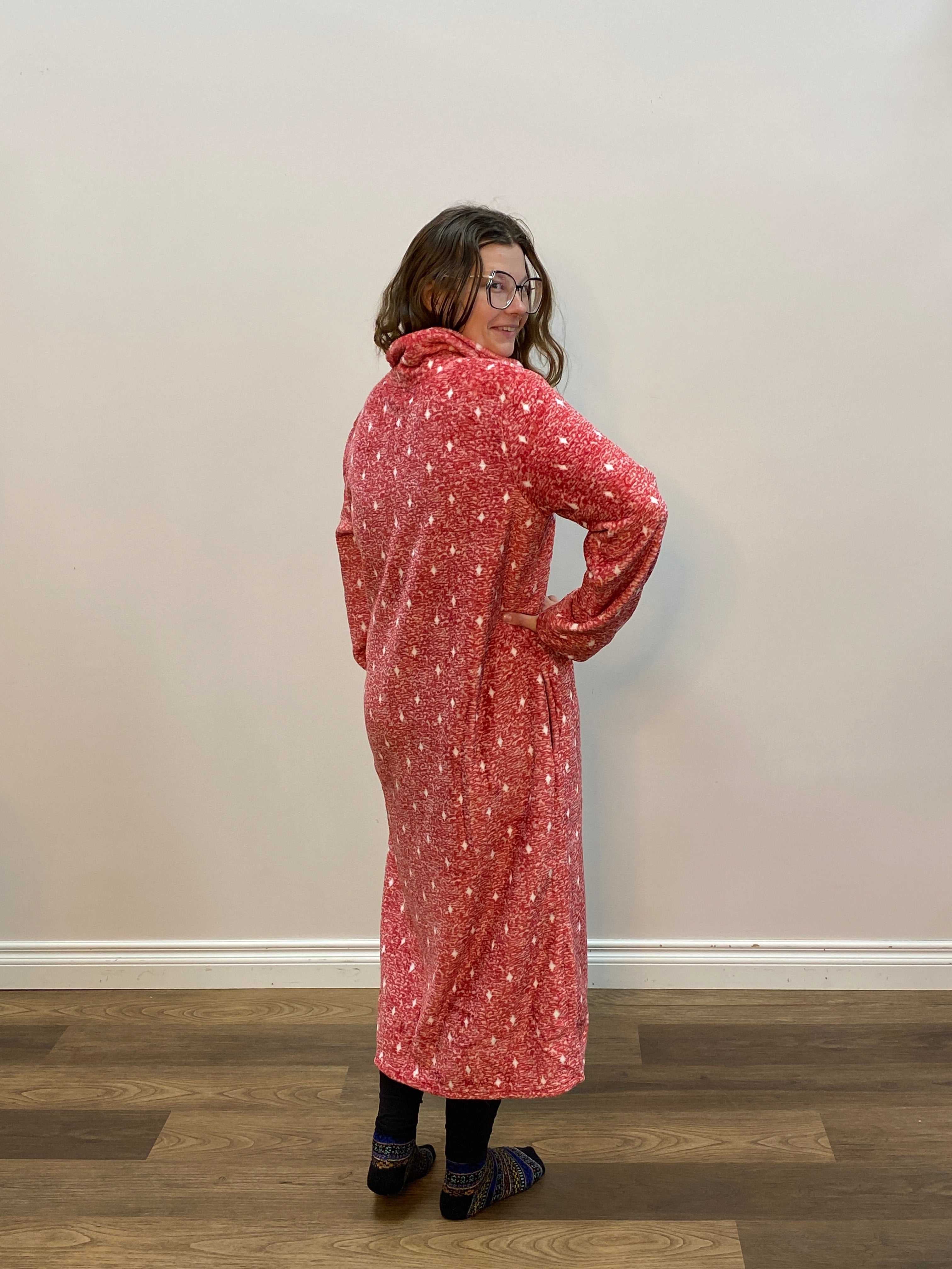 Person wearing a red patterned robe standing in front of a white wall.