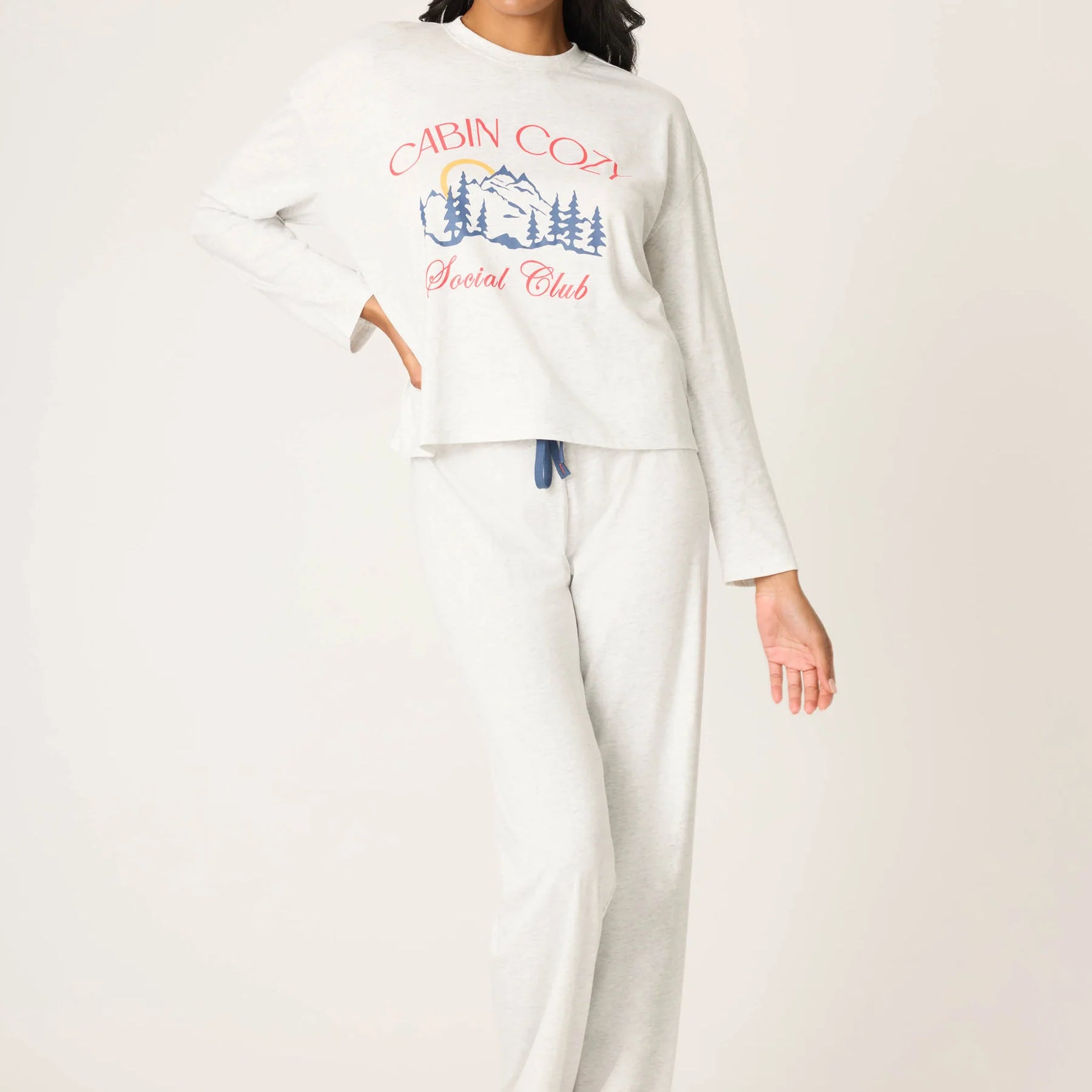 Woman wearing a white long-sleeve top and pants with a graphic design on a plain background