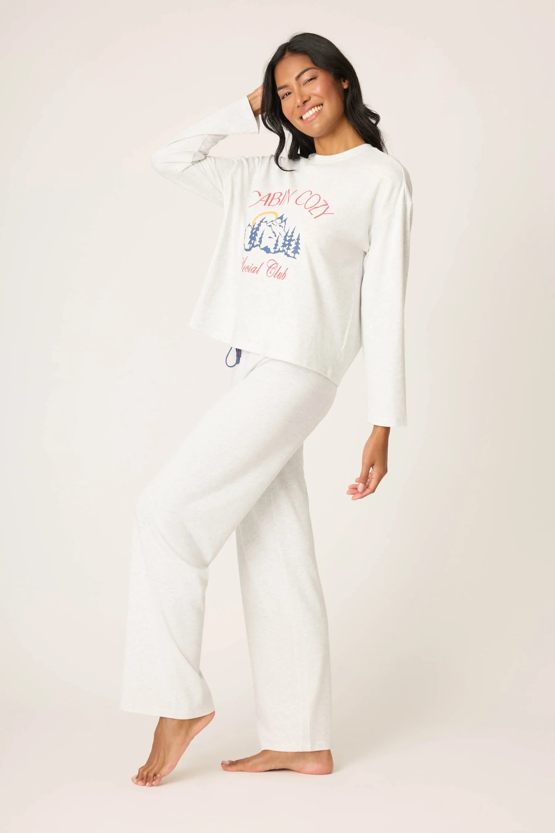 Woman wearing a white sweatshirt with colorful text and matching pants on a plain background
