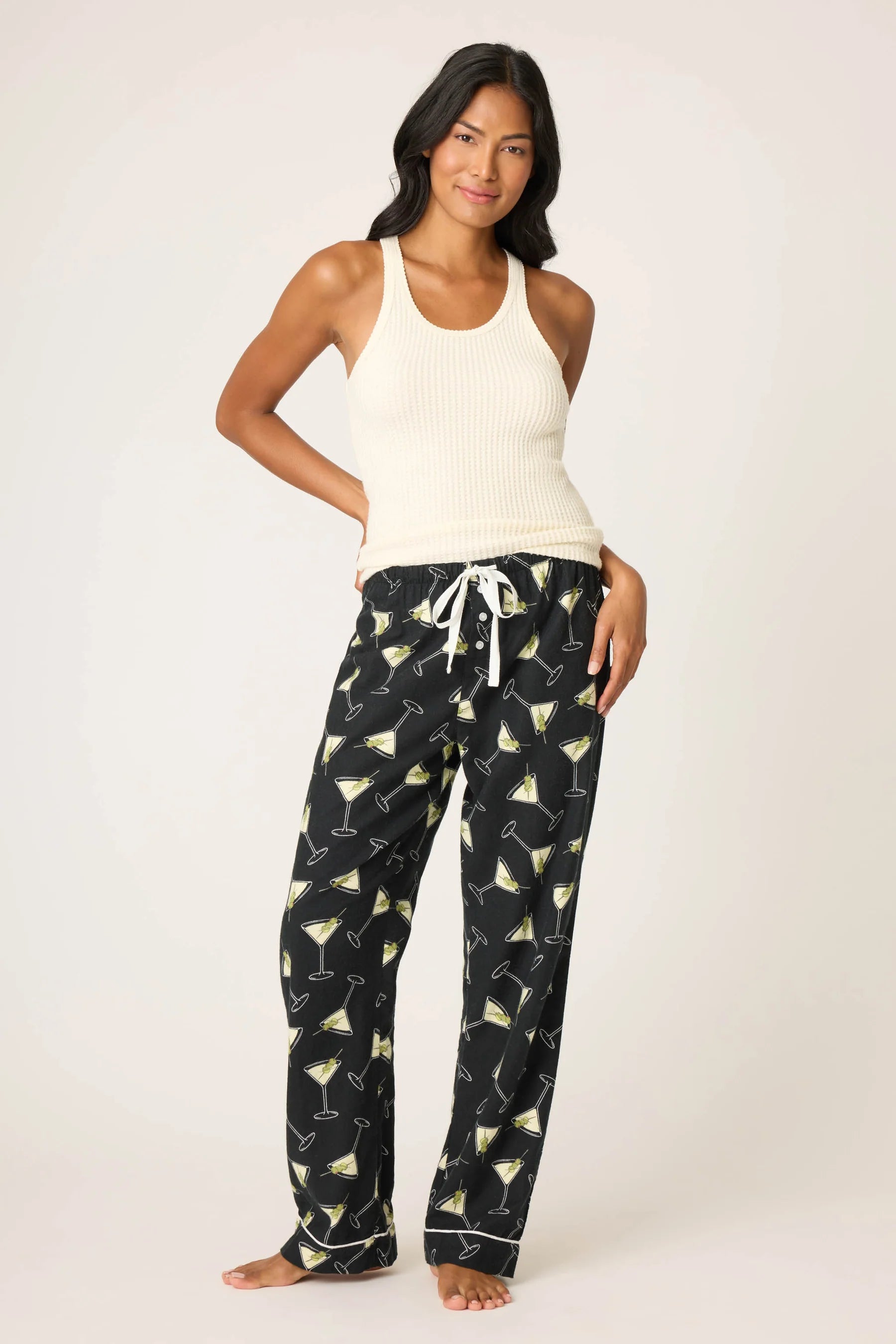 Woman wearing a white tank top and black pajama pants with cocktail pattern on a white background