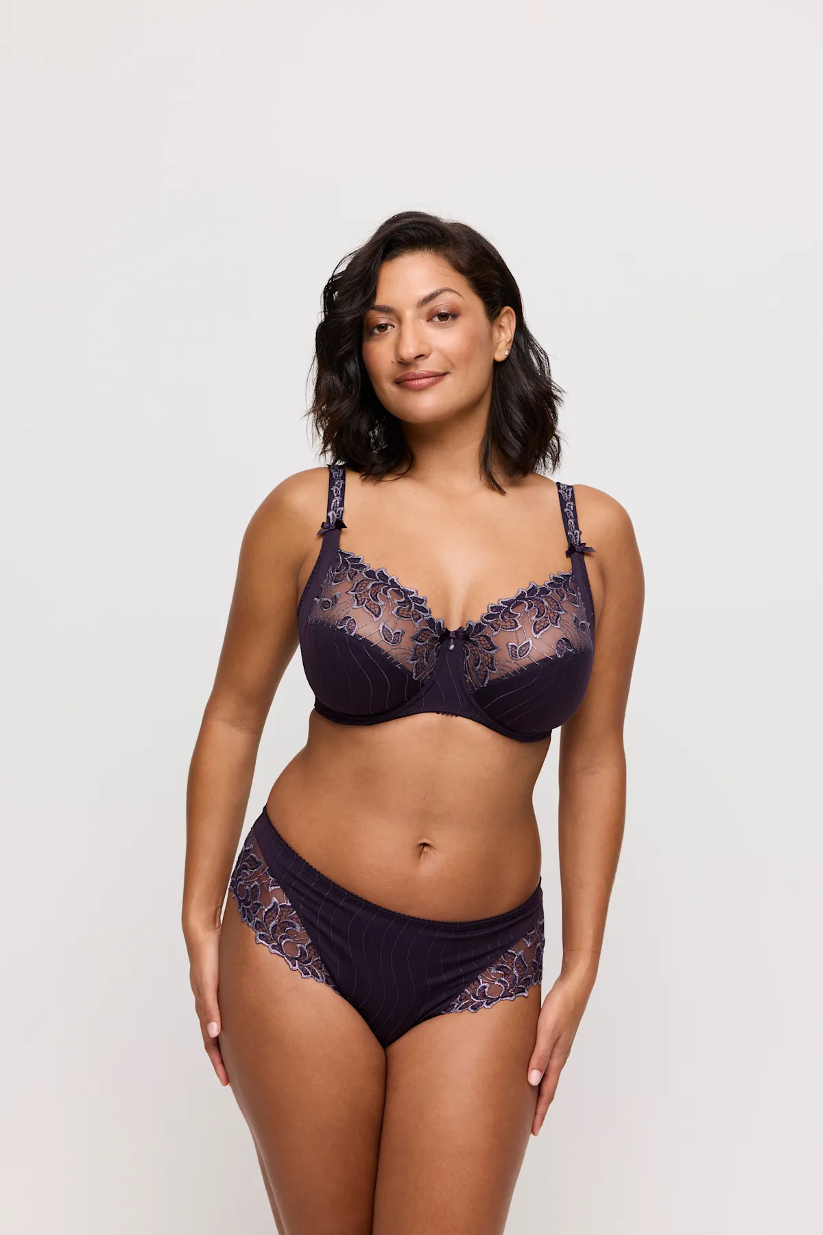 Woman wearing a dark purple lace lingerie set on a light background