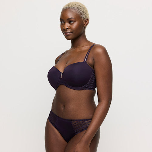 Woman wearing a dark purple bra and underwear set on a plain background