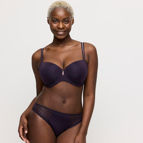 Woman wearing a dark purple bra and panties set on a plain background