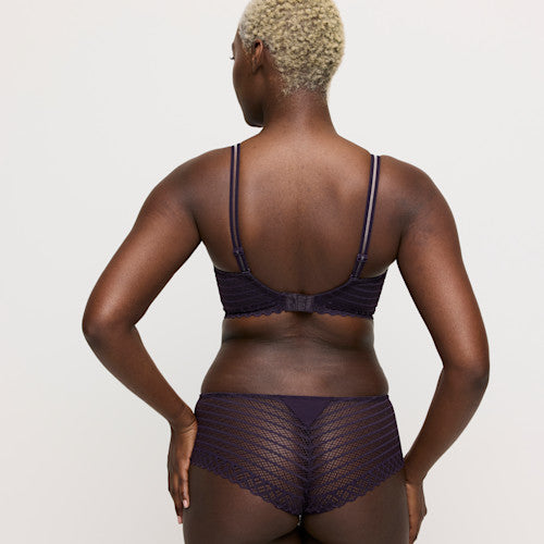 Person wearing a dark purple lingerie set on a plain background