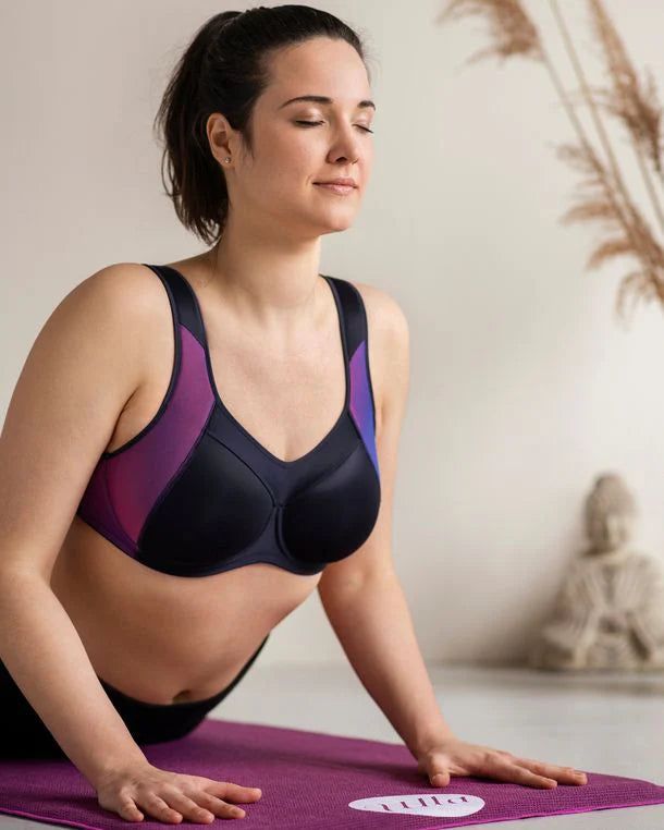 Woman in a black and purple sports bra on a yoga mat with a blurred background