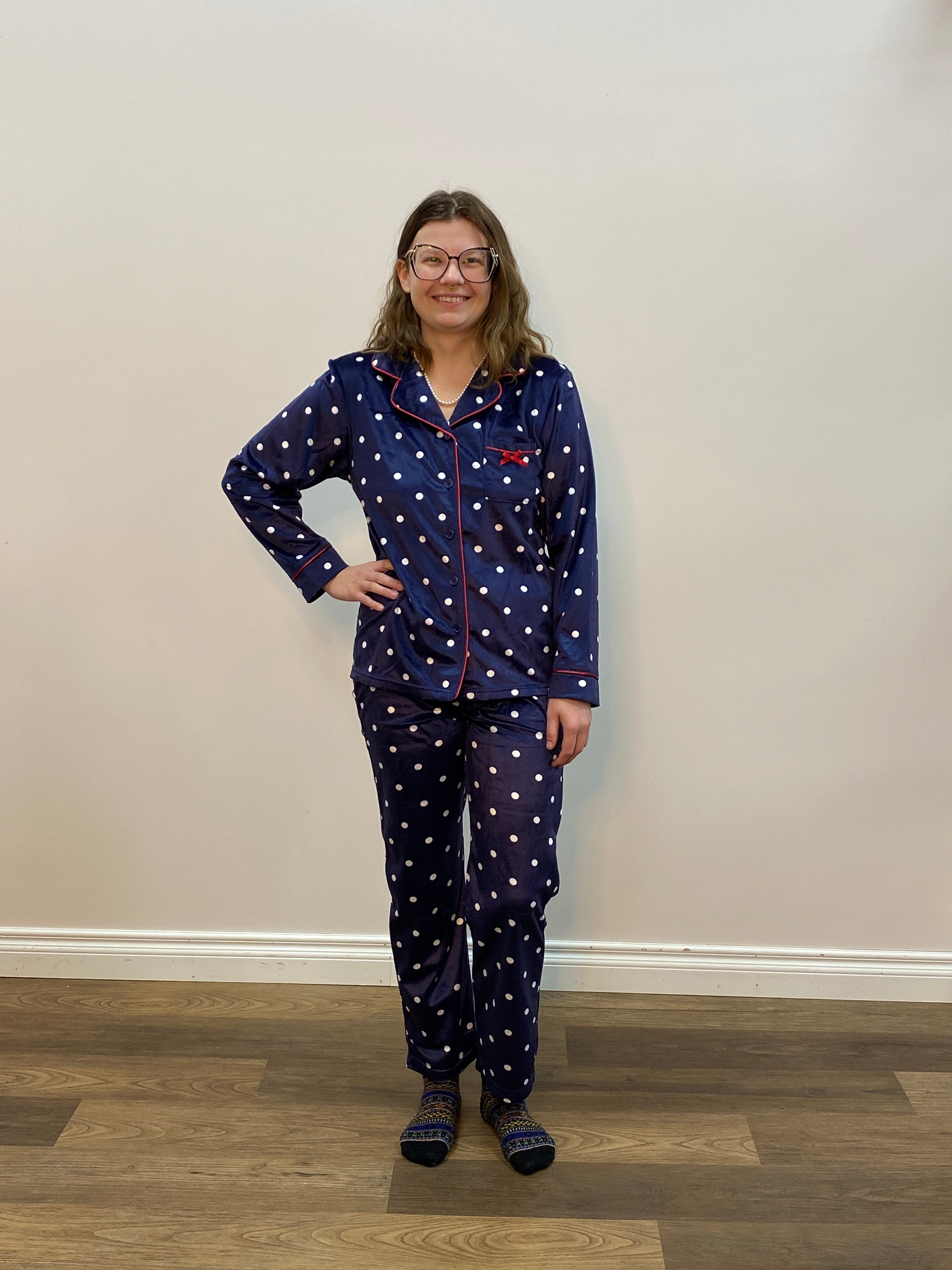 Person wearing a blue polka dot pajama set standing in a room with a white wall and wooden floor.