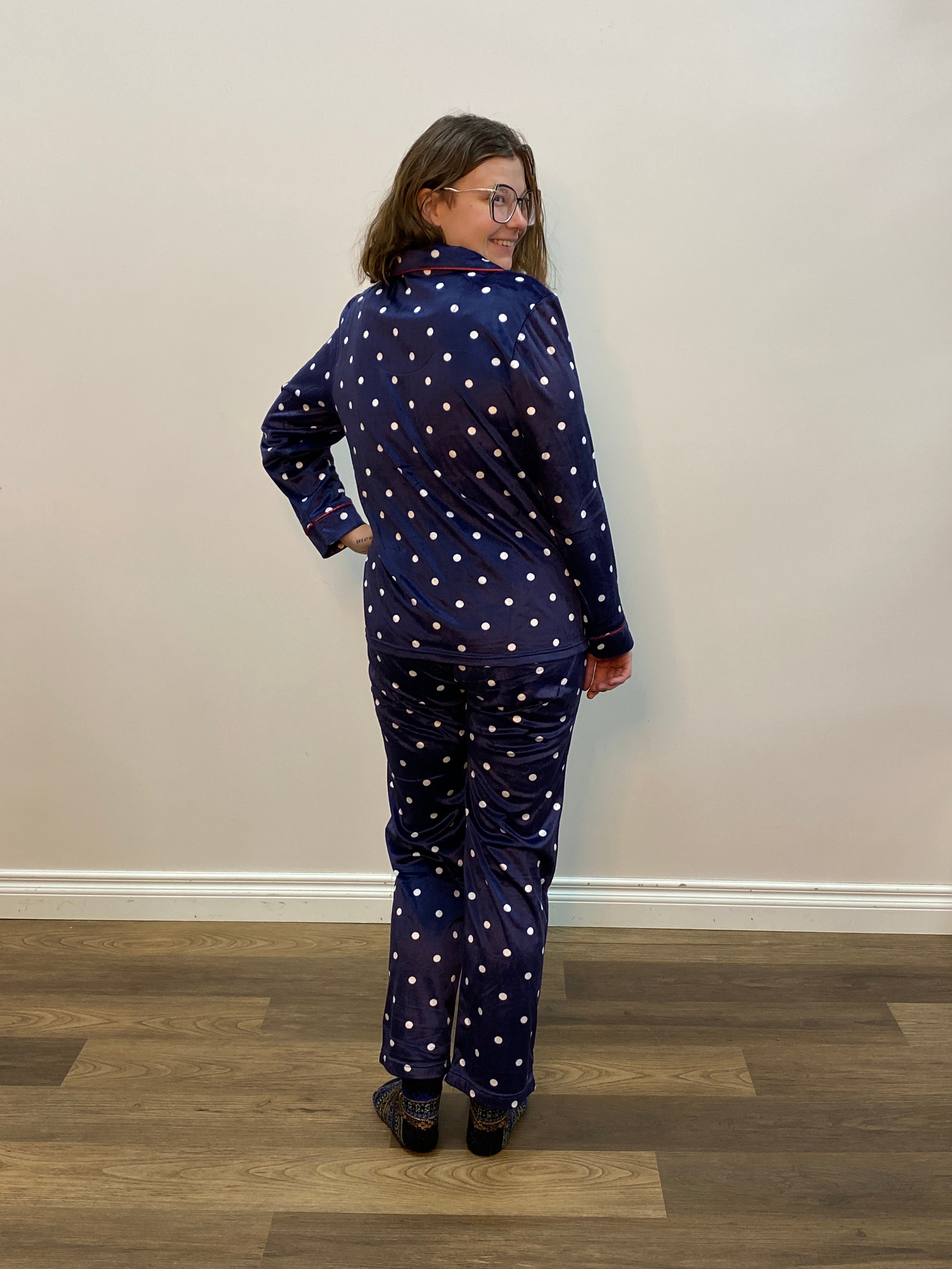 Person wearing a navy blue polka dot pajama set standing against a white wall.