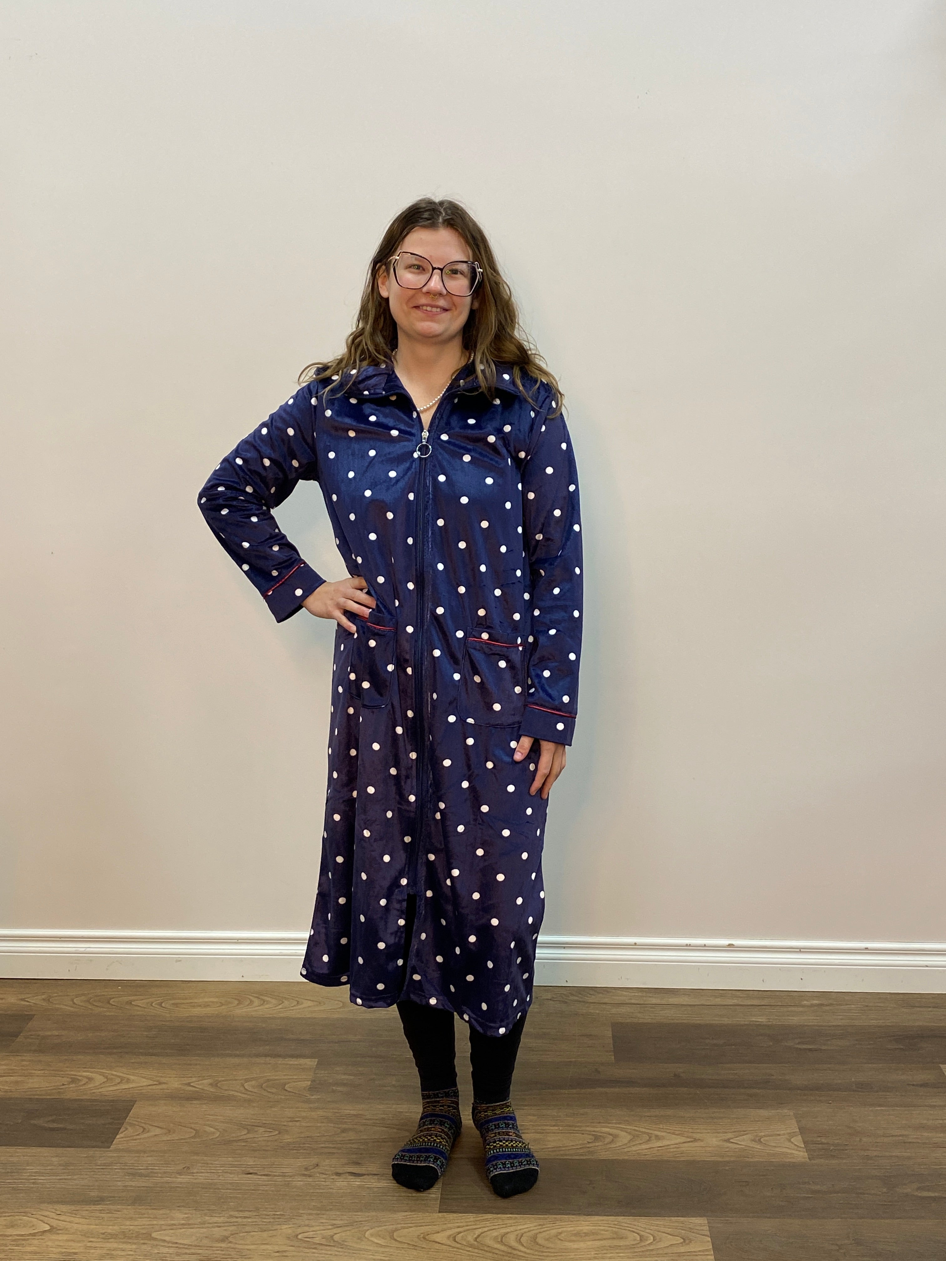 Person wearing a blue polka dot robe standing in a room with a white wall and wooden floor.