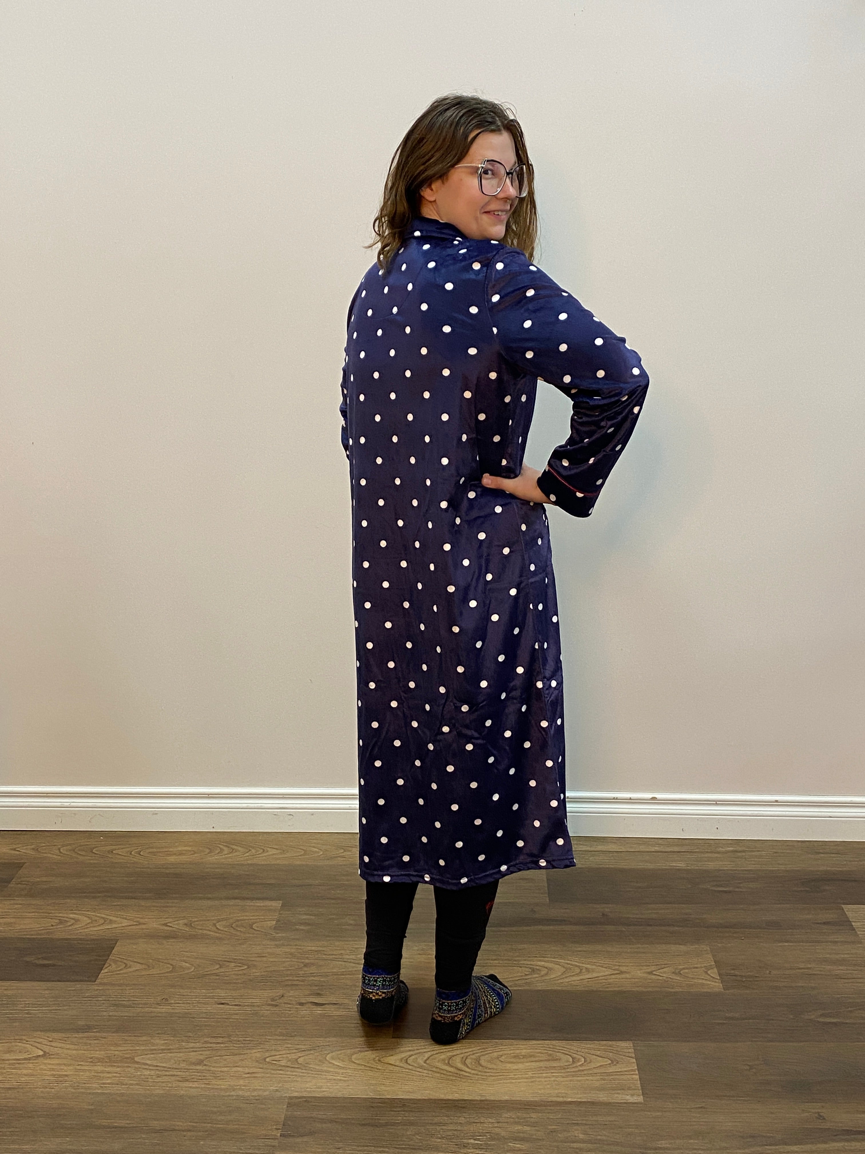 Person wearing a navy blue robe with white polka dots in a minimal indoor setting.
