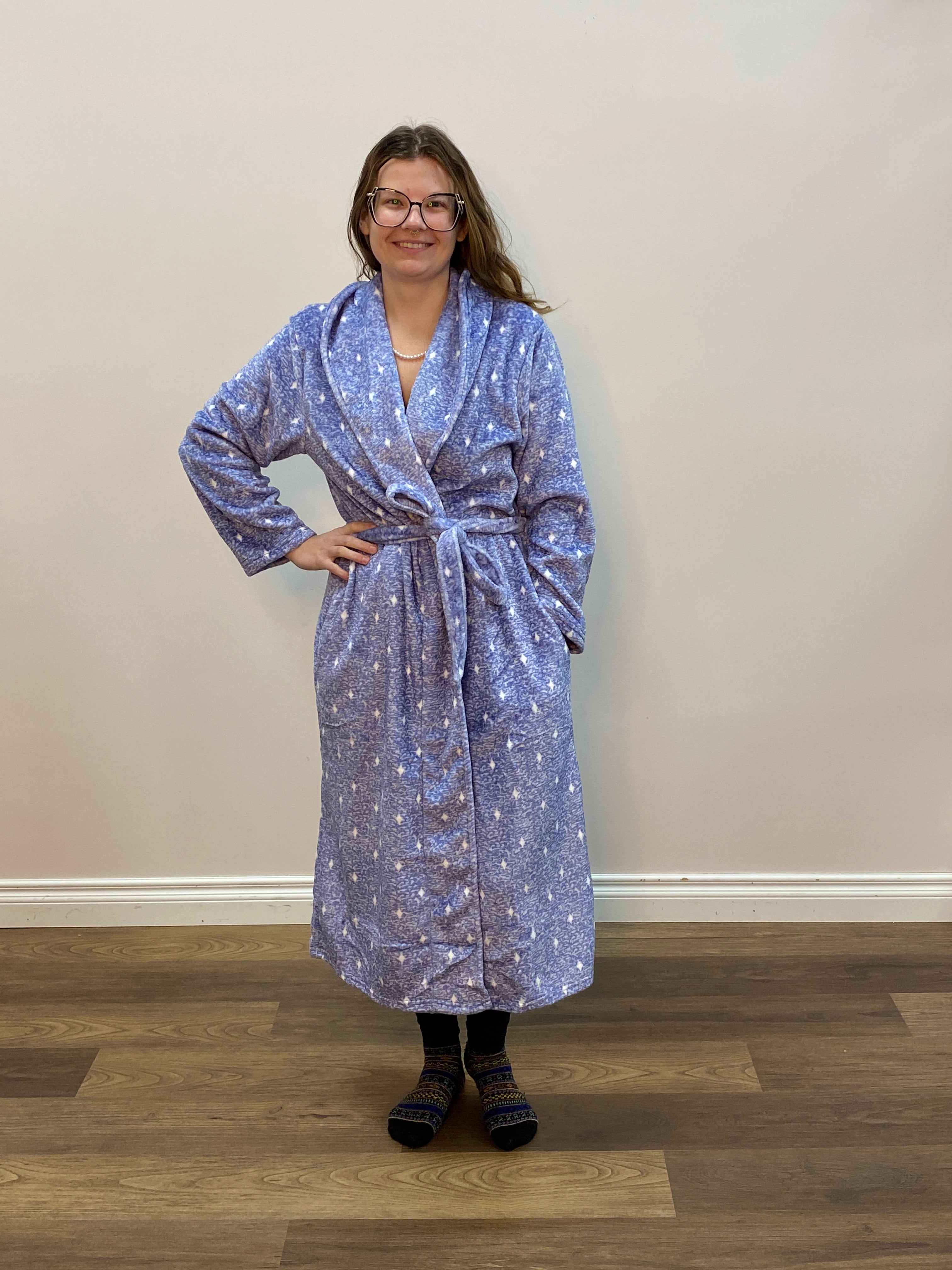 Person wearing a blue patterned robe standing against a white wall.