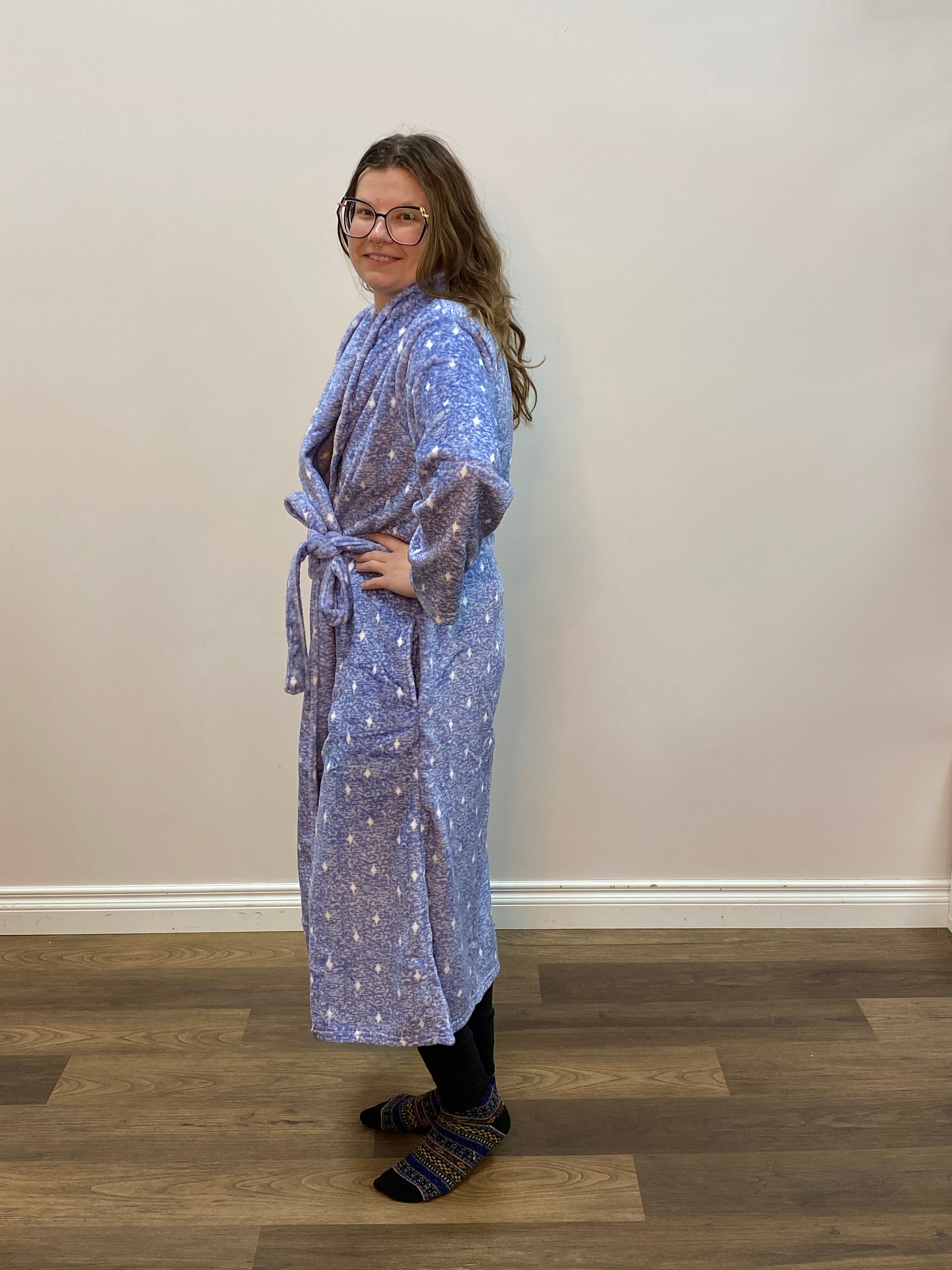 Person wearing a blue patterned robe standing against a white wall.
