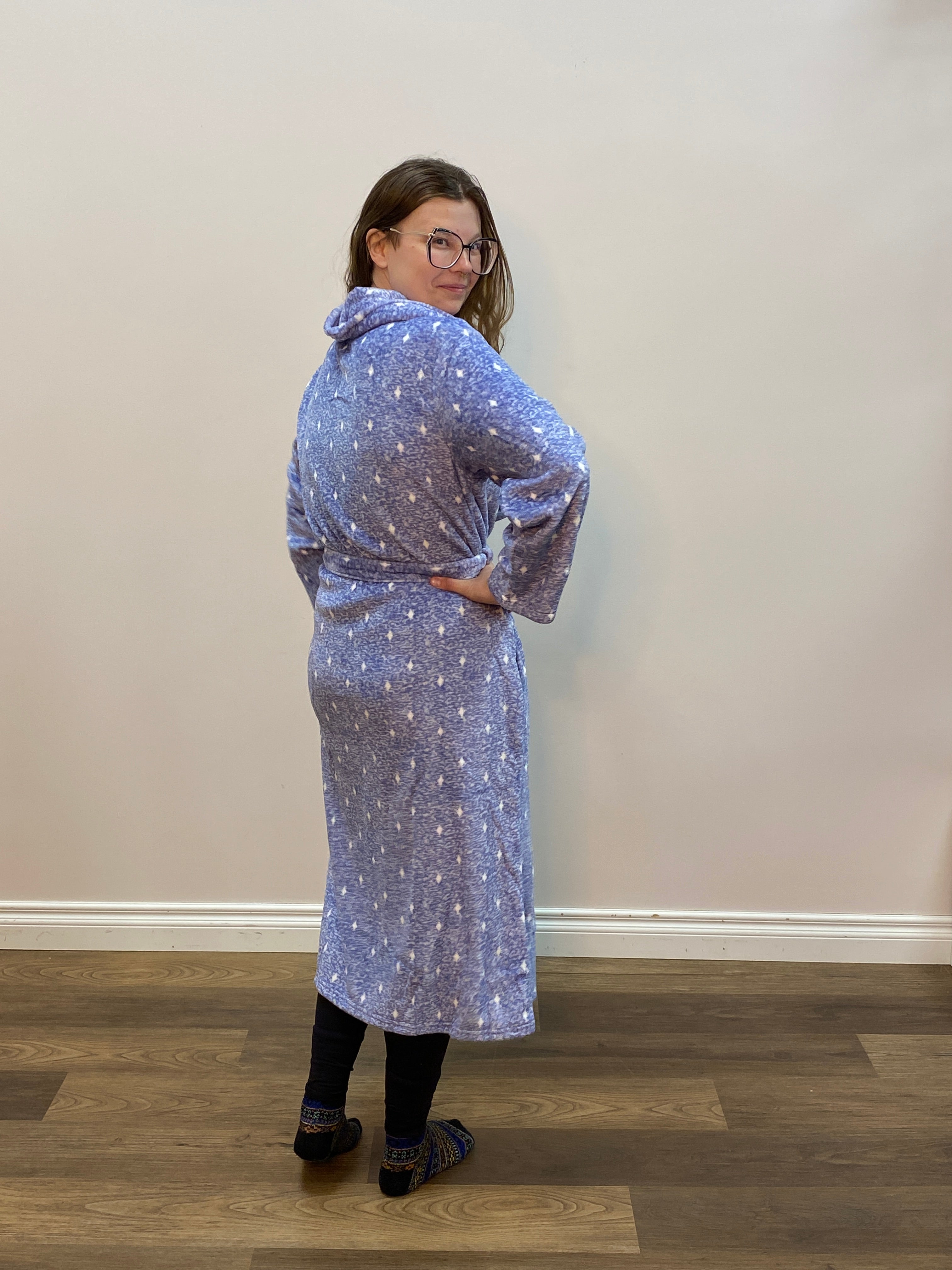 Person wearing a long-sleeve, patterned robe standing against a plain wall.