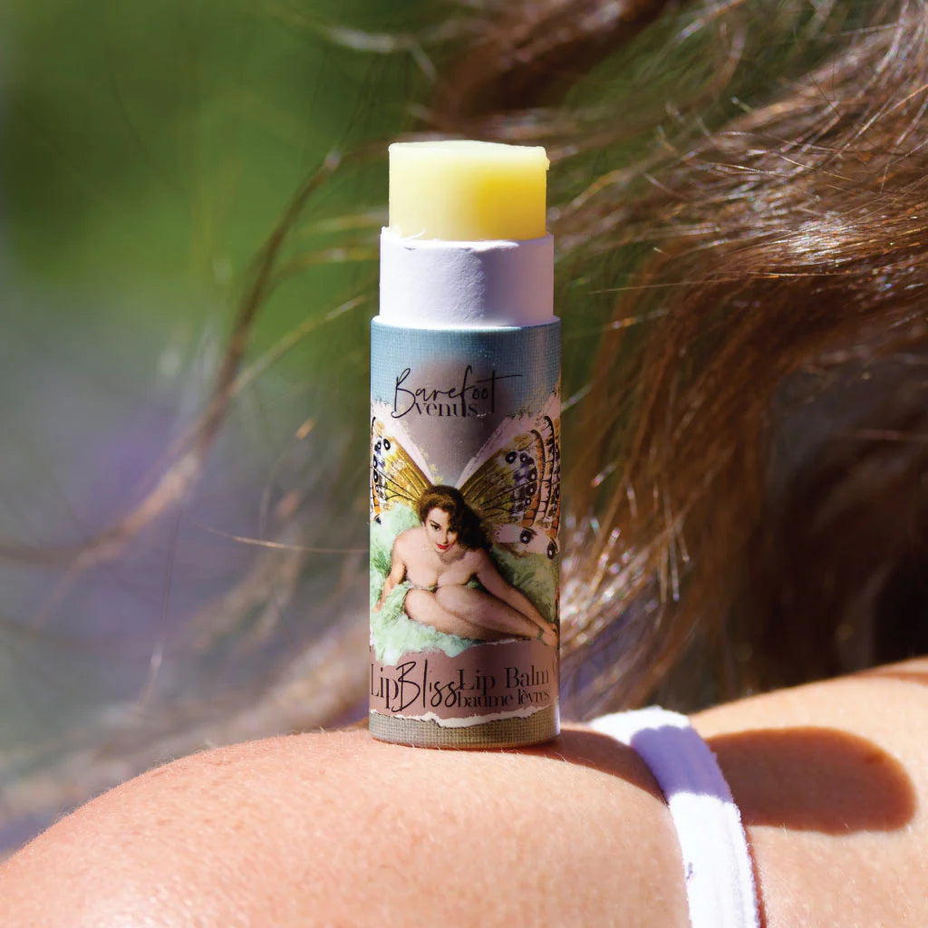 Barefoot Venus Lip Bliss Balm tube with fairy design on a person's shoulder against a blurred natural background