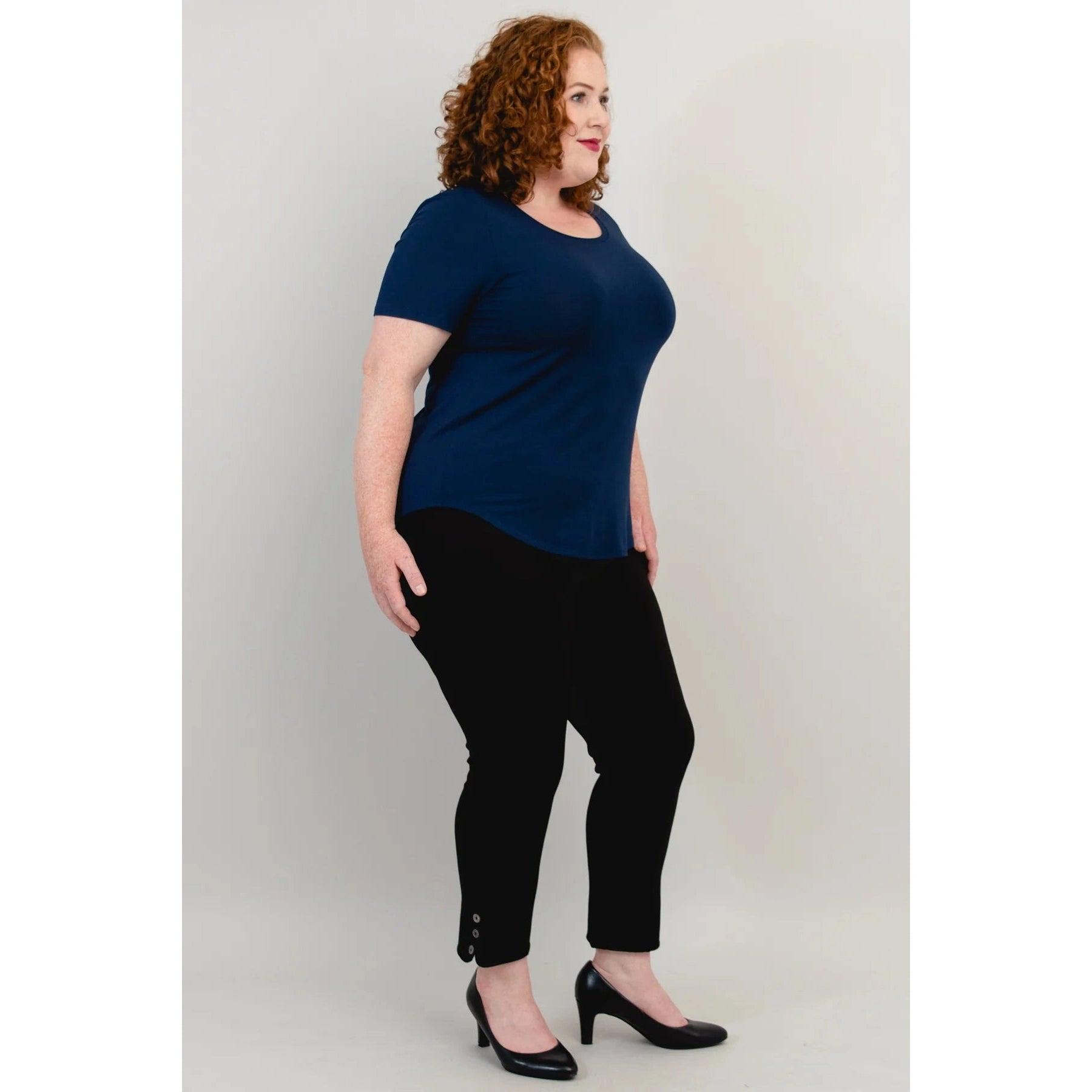 Blue Sky Tessa Tee in Indigo shown on a model wearing black leggings standing against a white background, from the side view.