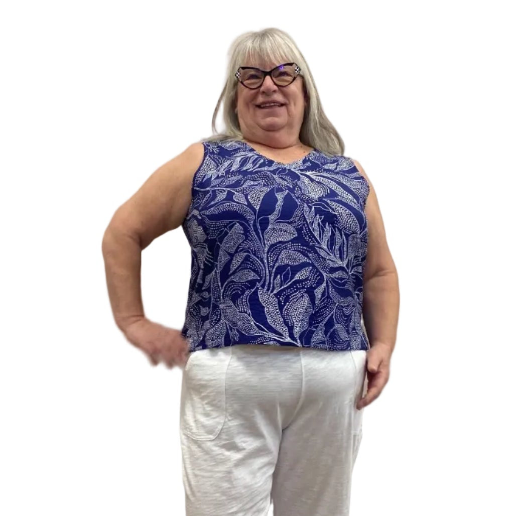 Woman wearing the blue and white floral Escape Resort tank against a white background, paired with white pants.