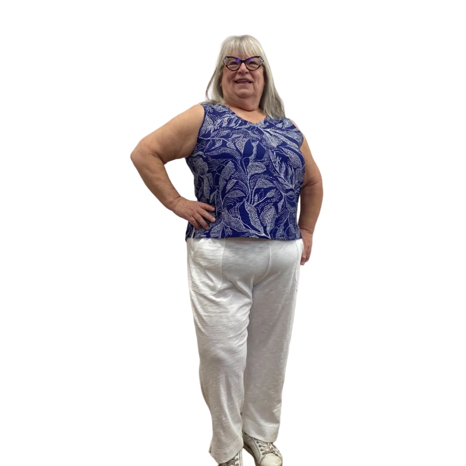 Woman wearing the blue and white floral Escape Resort tank against a white background, paired with white pants.