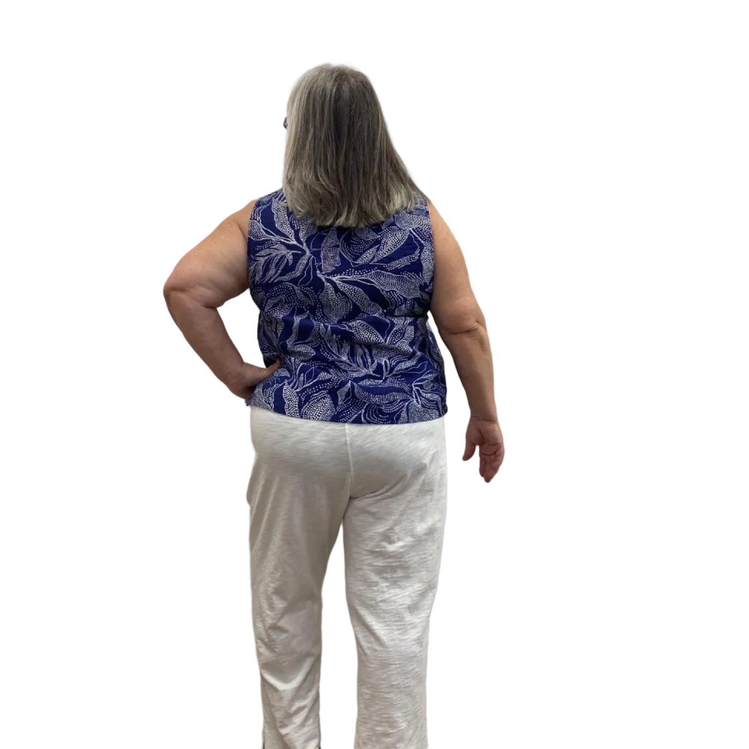 Woman wearing the blue and white floral Escape Resort tank against a white background, paired with white pants.