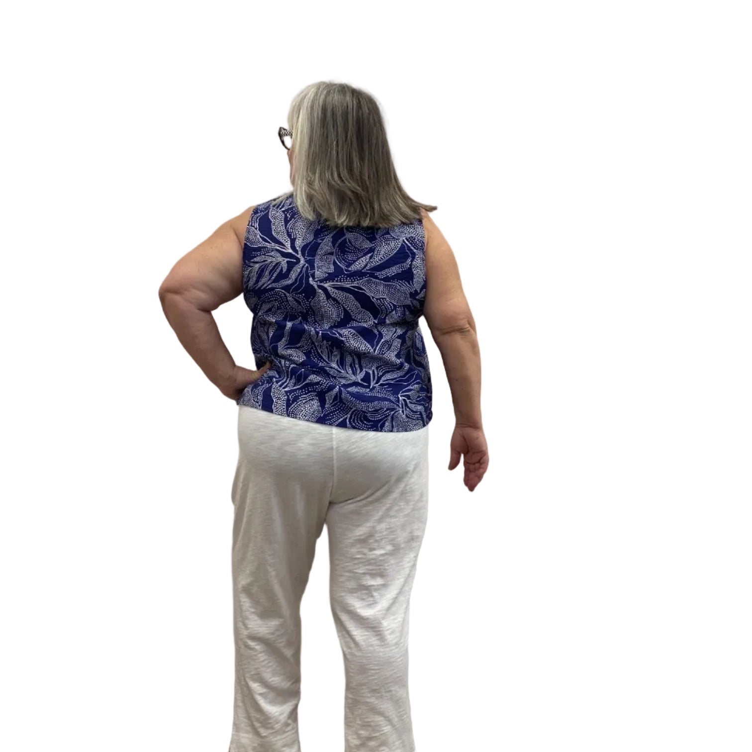 Woman wearing the blue and white floral Escape Resort tank against a white background, paired with white pants.