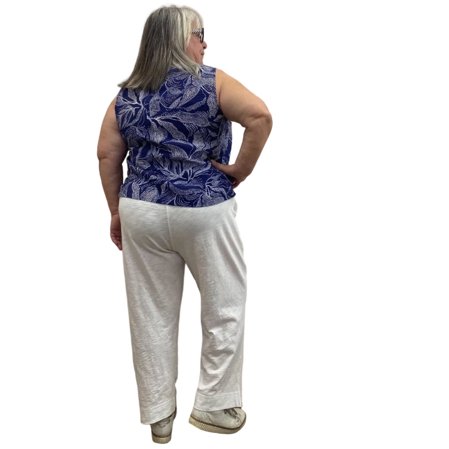 Woman wearing the blue and white floral Escape Resort tank against a white background, paired with white pants.