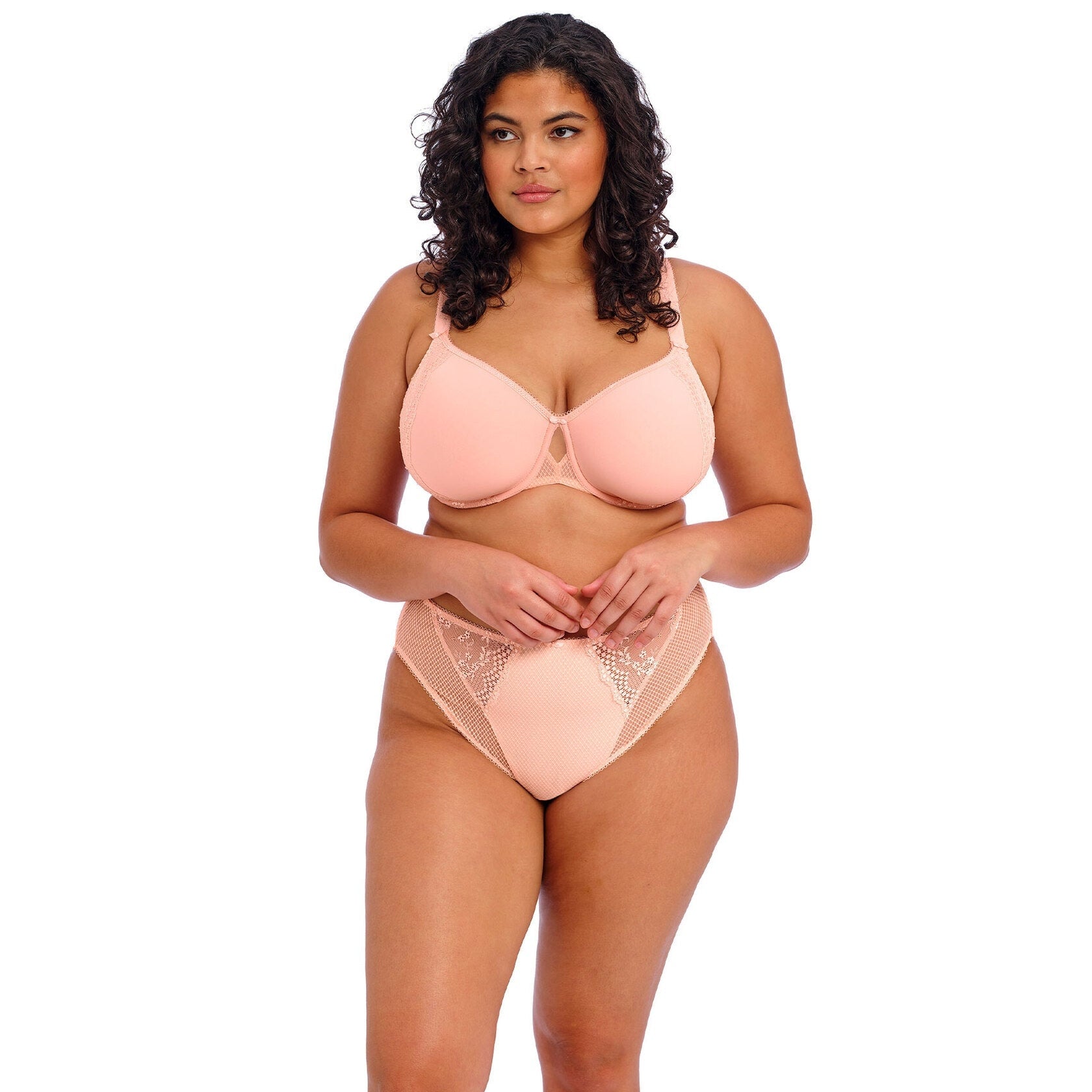 A woman wearing a light pink bra and panty set against a white back ground. 