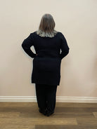 Person wearing a black outfit standing against a plain wall.
