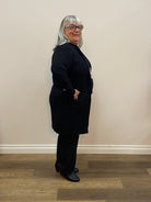 Person wearing a black sweater standing against a plain wall.