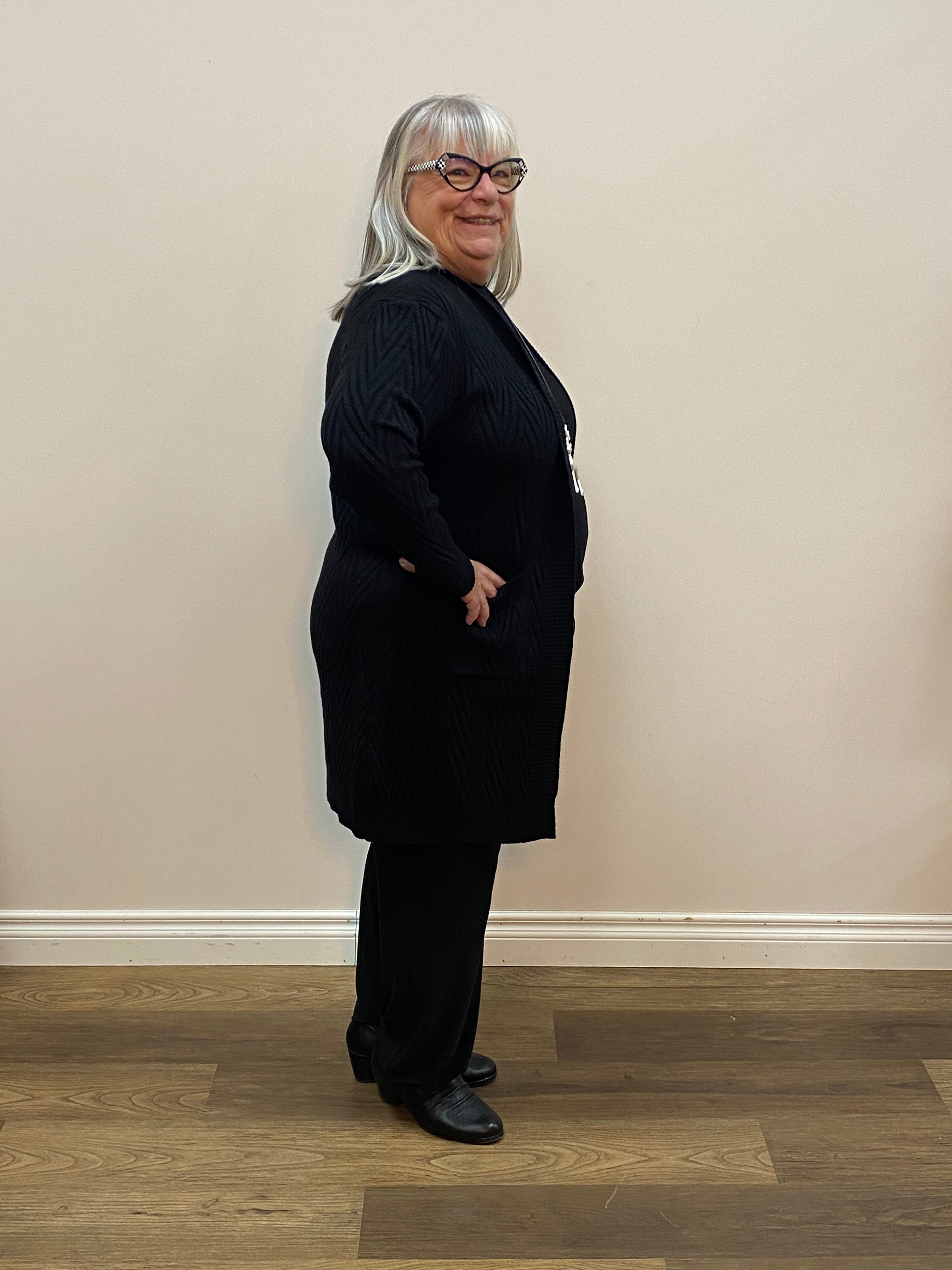 Person wearing a black sweater standing against a plain wall.