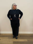 Person wearing a black outfit with a white necklace in front of a mirror.