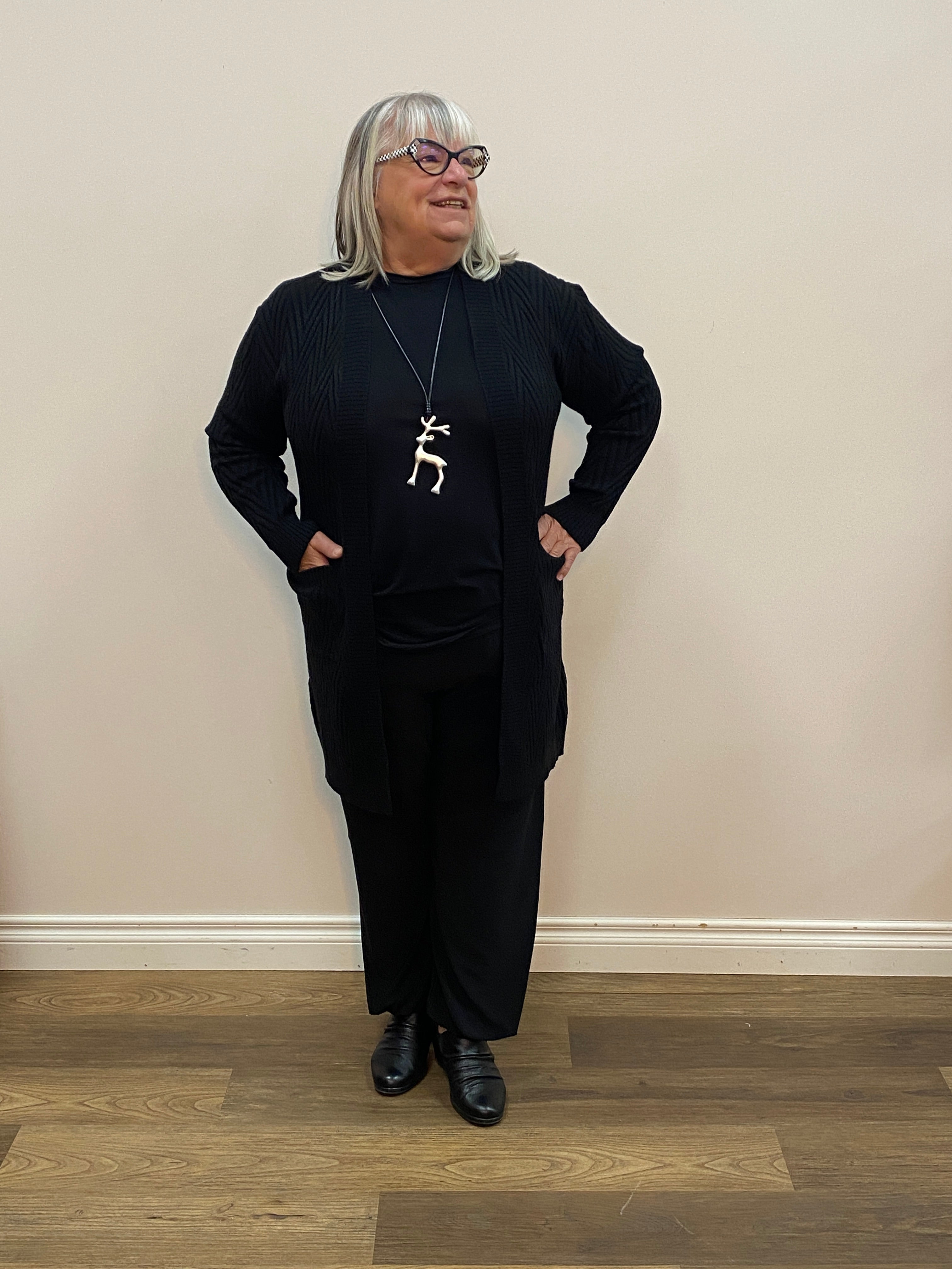 Person wearing a black outfit with a white necklace in front of a mirror.