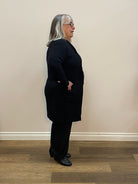 Person wearing a black outfit standing against a light-colored wall.