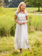 Woman in a white dress with black patterns standing in a grassy field.