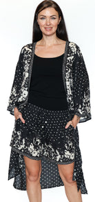 Woman wearing a black and white floral kimono-style jacket over a black top and skirt on a white background