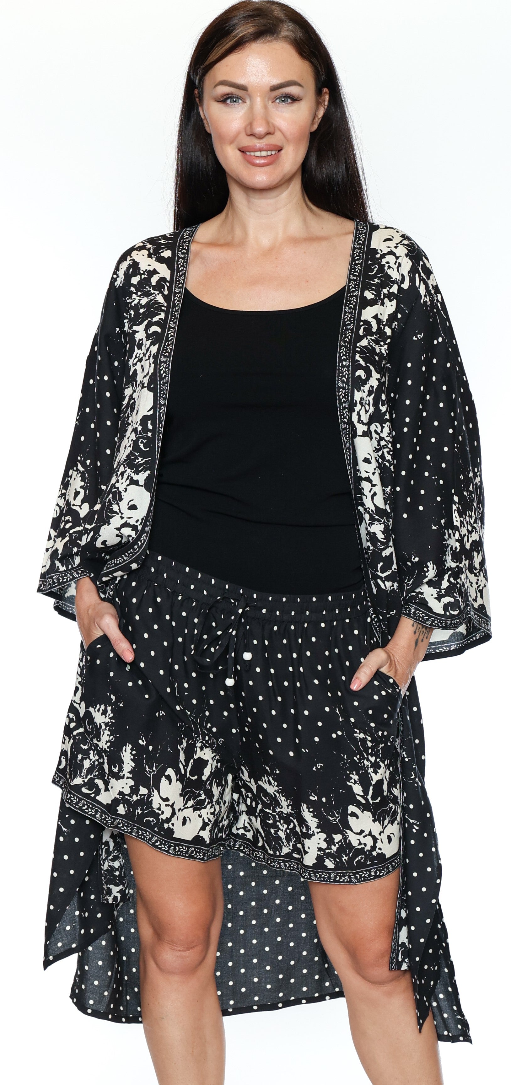 Woman wearing a black and white floral kimono-style jacket over a black top and skirt on a white background