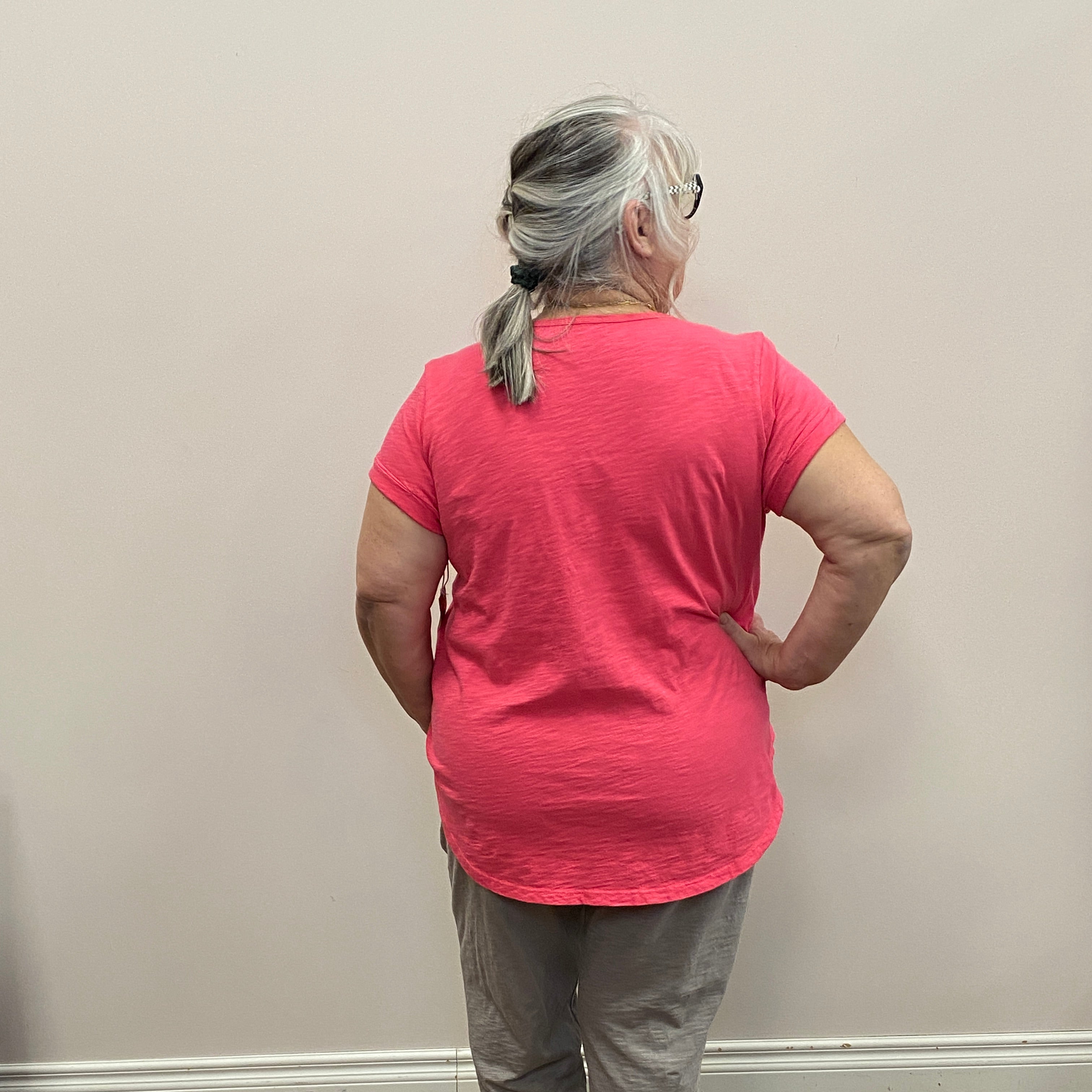 Person in a pink shirt and gray pants standing in front of a mirror on a wooden floor.