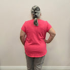 Person wearing a pink shirt and gray pants standing against a plain wall.