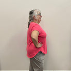 Person in a pink shirt and gray pants standing against a plain wall.